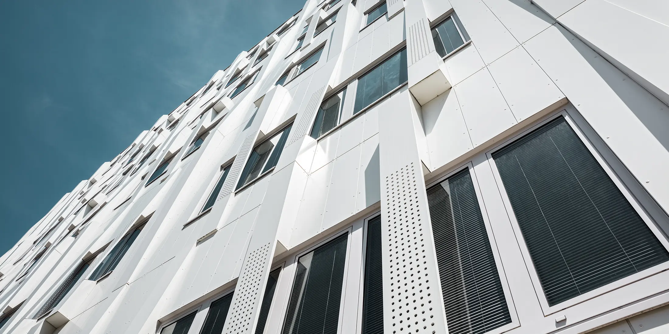 Nahaufnahme der 3D-Fassade mit gelochten Aluminium Verbundplatten-Kassetten und normalen PREFA Verbundplatten in Reinweiß. Die Kassettenfassade von PREFA macht das Gebäude zu einem Blickfang.