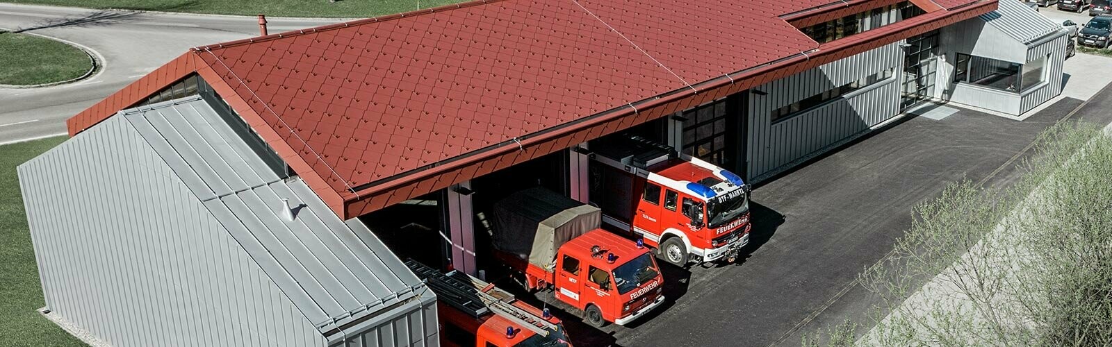 Véhicules de pompiers dans la caserne de la société PREFA. Le bâtiment est doté d’une toiture en losanges rouges (aluminium non inflammable) et d’une façade en aluminium.