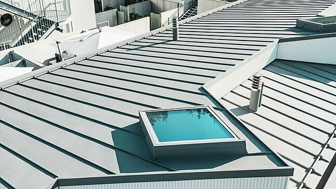 L'immagine mostra un edificio moderno con un tetto PREFALZ. Il tetto è realizzato in alluminio ondulato, con finestre integrate e una facciata strutturata.