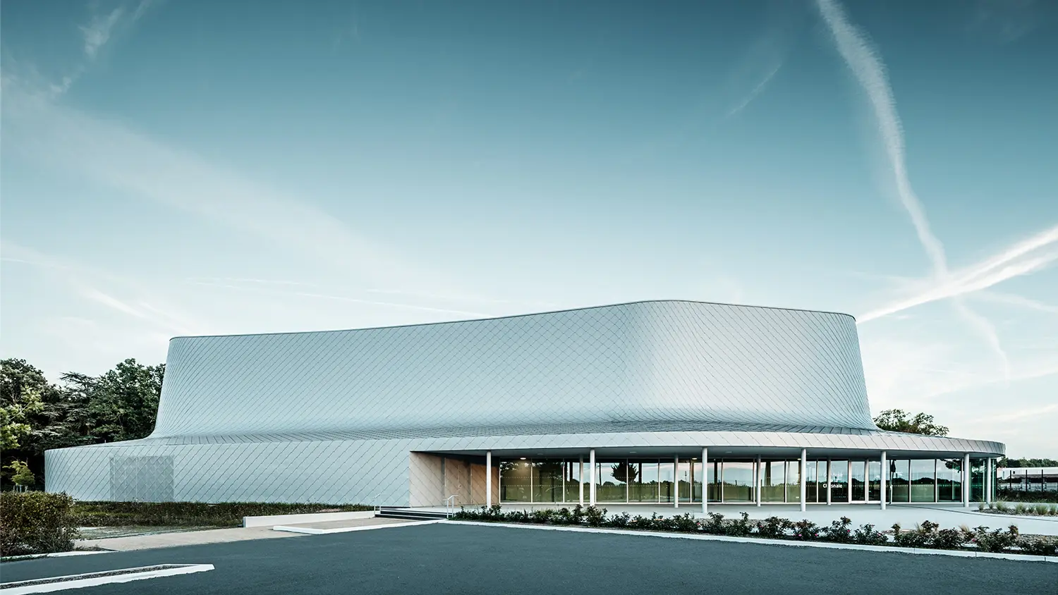 Vue latérale du bâtiment incluant le parvis. Le vitrage de la zone d'entrée donne l'impression que le bâtiment est partiellement transparent.