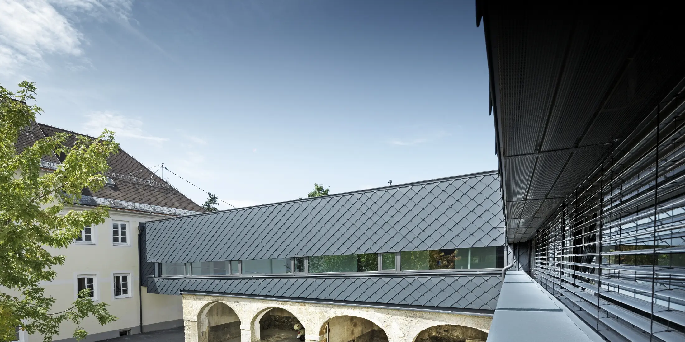 Il piano superiore dell'edificio storico è stato rivestito con la scaglia per facciata PREFA 29 nel colore antracite, in modo che le vecchie strutture al piano terra si armonizzino perfettamente con le nuove scaglie.