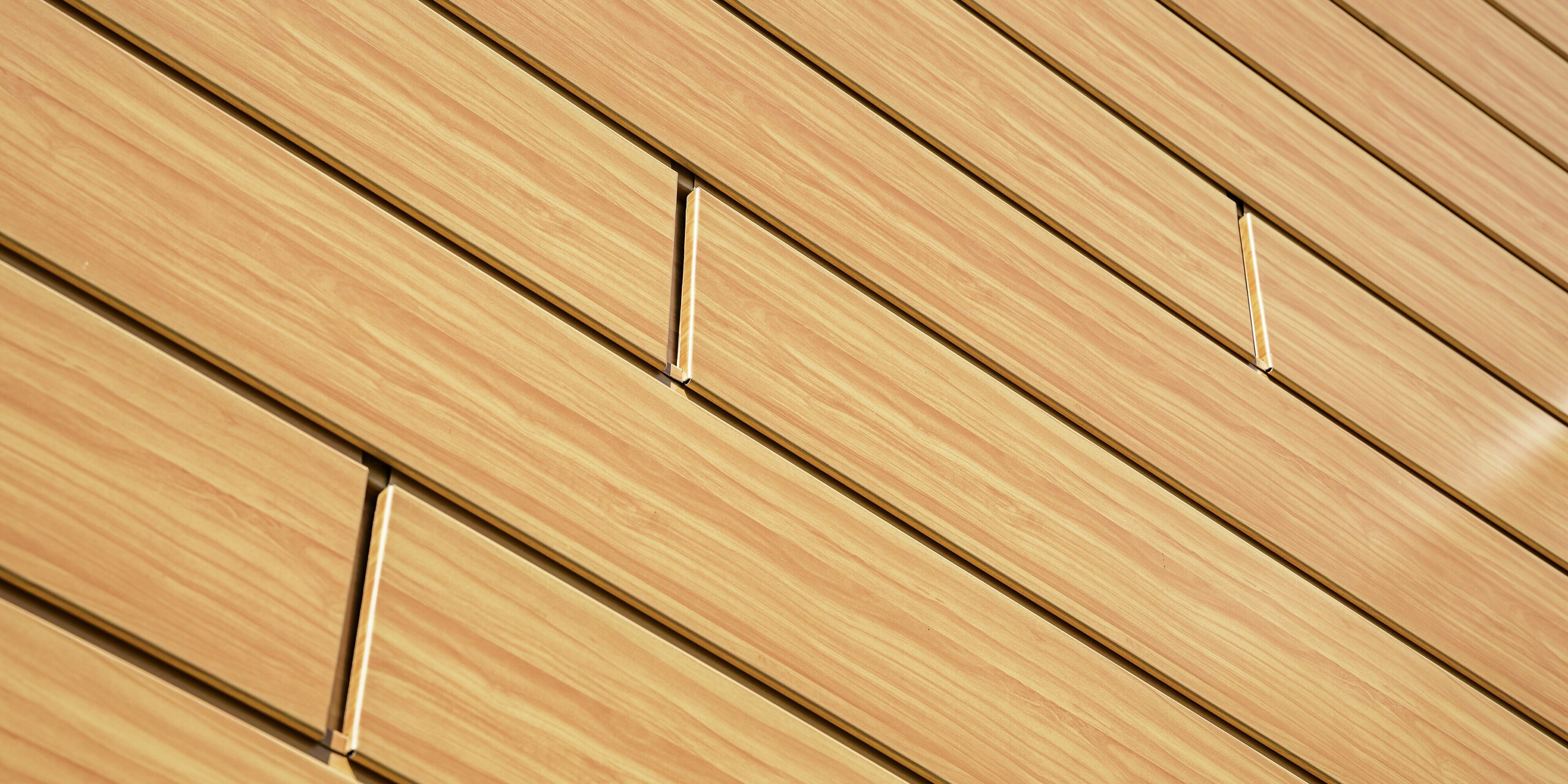 Gros plan sur les Sidings PREFA en chêne naturel. Ce revêtement en aluminium de haute qualité imite à la perfection le bois, avec un grain fin et une teinte chaleureuse. Les lignes précises des panneaux créent un effet de surface moderne et apaisant, et mettent en valeur la douce lumière. Durables, résistants aux intempéries, inaltérables et quasiment sans entretien, les bardages PREFA constituent une solution esthétique et fonctionnelle idéale pour les rénovations de façades exigeantes.Gros plan sur les Sidings PREFA en chêne naturel. Ce revêtement en aluminium de haute qualité imite à la perfection le bois, avec un grain fin et une teinte chaleureuse. Les lignes précises des panneaux créent un effet de surface moderne et apaisant, et mettent en valeur la douce lumière. Durables, résistants aux intempéries, inaltérables et quasiment sans entretien, les bardages PREFA constituent une solution esthétique et fonctionnelle idéale pour les rénovations de façades exigeantes.