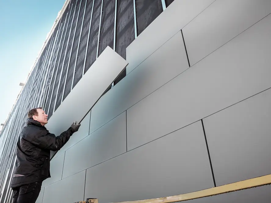 Ein Handwerker deckt eine Fassade mit Sidings ein.