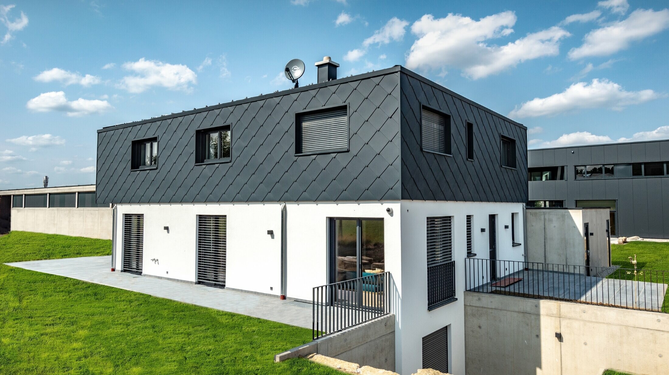 Schlichter Neubau mit Flachdach, das Erdgeschoß ist weiß verputzt, das Obergeschoß ist mit der großen PREFA Wandraute in Anthrazit verkleidet.