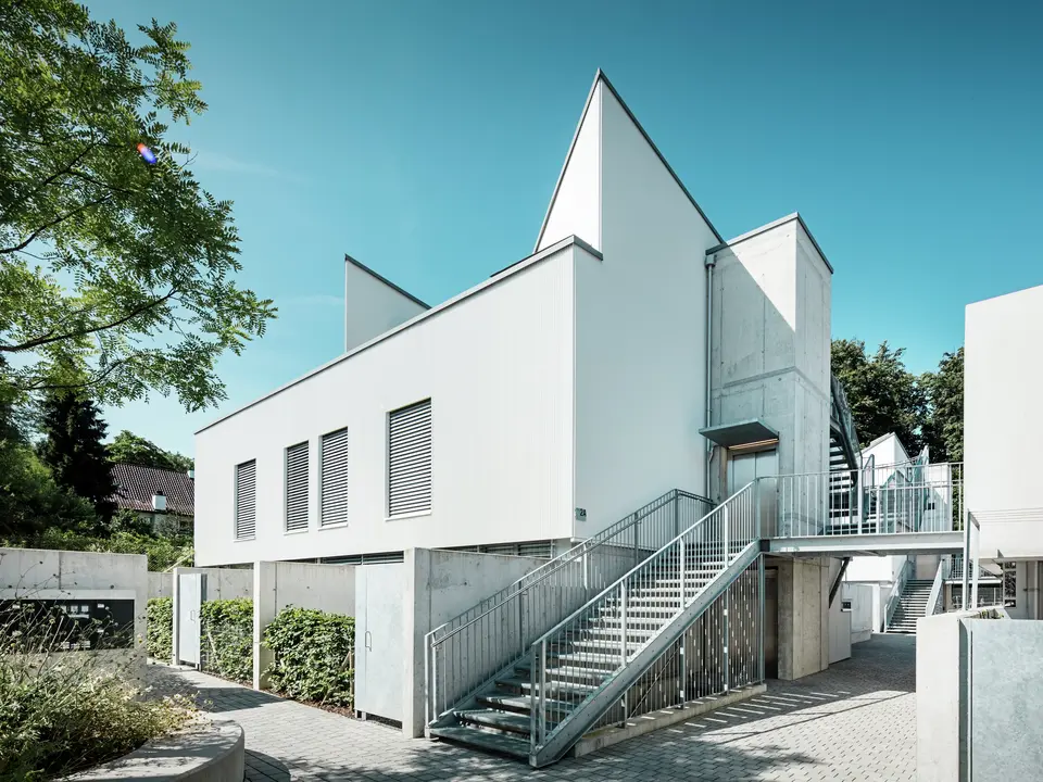 Ensemble moderner Tiny Homes mit markanten Spitzdächern, verkleidet mit dem PREFA Zackenprofil in der Farbe P.10 Reinweiß. Die schlichte, klare Fassadengestaltung harmoniert mit den Sichtbetonelementen und der umlaufenden Stahlkonstruktion. Die langlebige PREFA Aluminiumfassade schützt zuverlässig vor Witterung und sorgt für eine wartungsarme, ästhetisch reduzierte Optik.