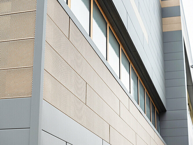 Les panneaux de façade de PREFA, Siding, sont désormais également disponibles en versions perforées : ici les éléments perforés couleur sable sont combinés à des panneaux gris. 