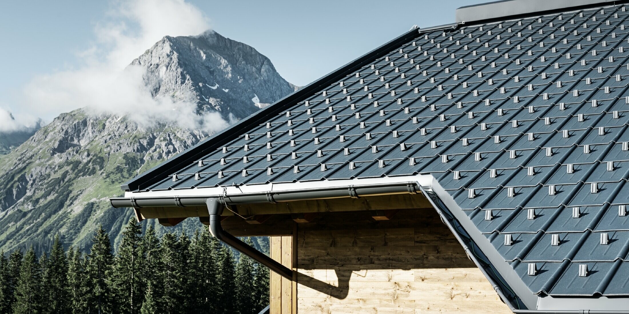 Casa di montagna in legno, il tetto è coperto con tegole PREFA antracite con grondaie PREFA e facciata in legno