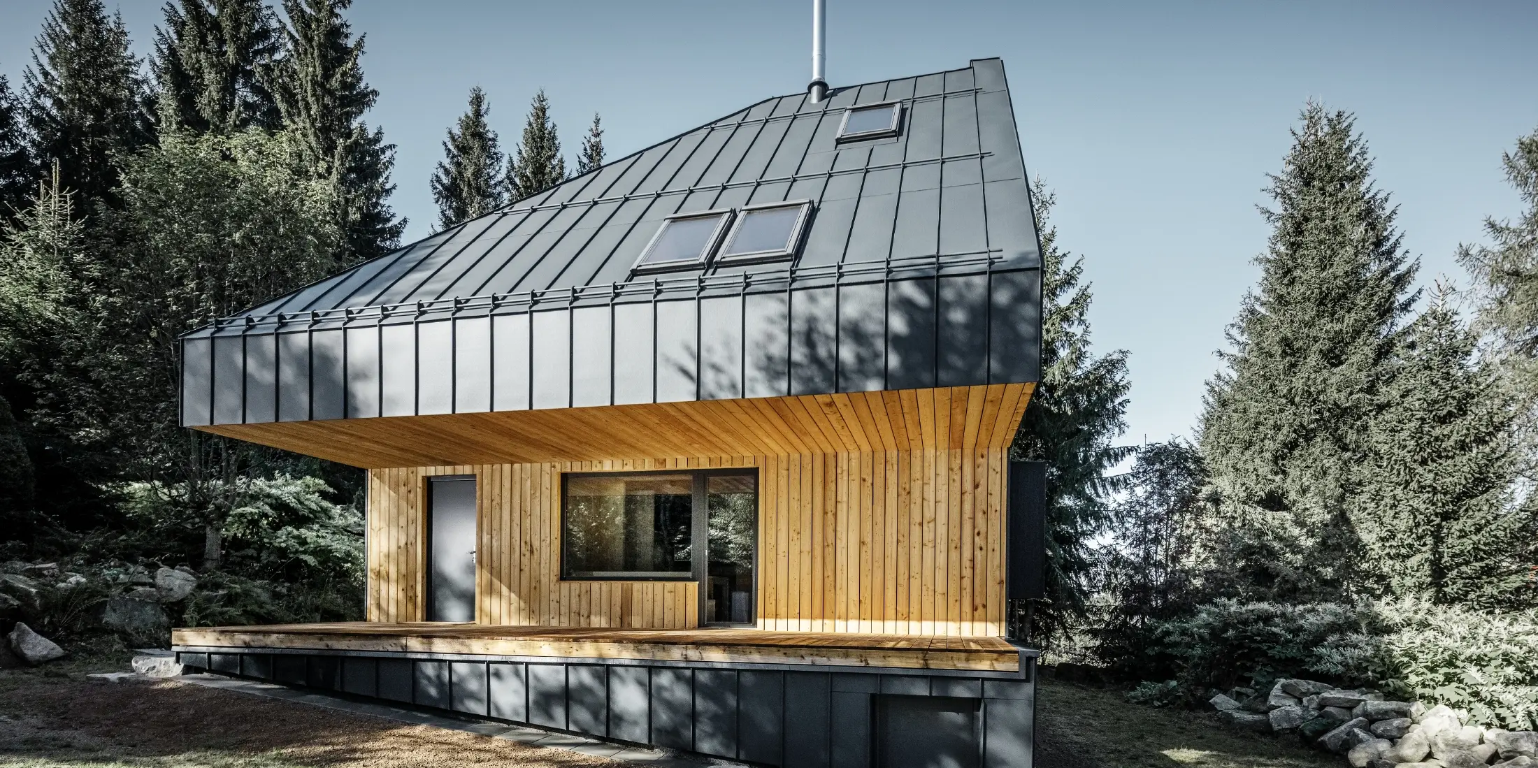 Casa unifamiliare moderna nel bosco, l'imponente tetto è stato rivestito con Prefalz in alluminio di PREFA in antracite. La vista dal basso e la facciata sono rivestite con pannelli di legno.
