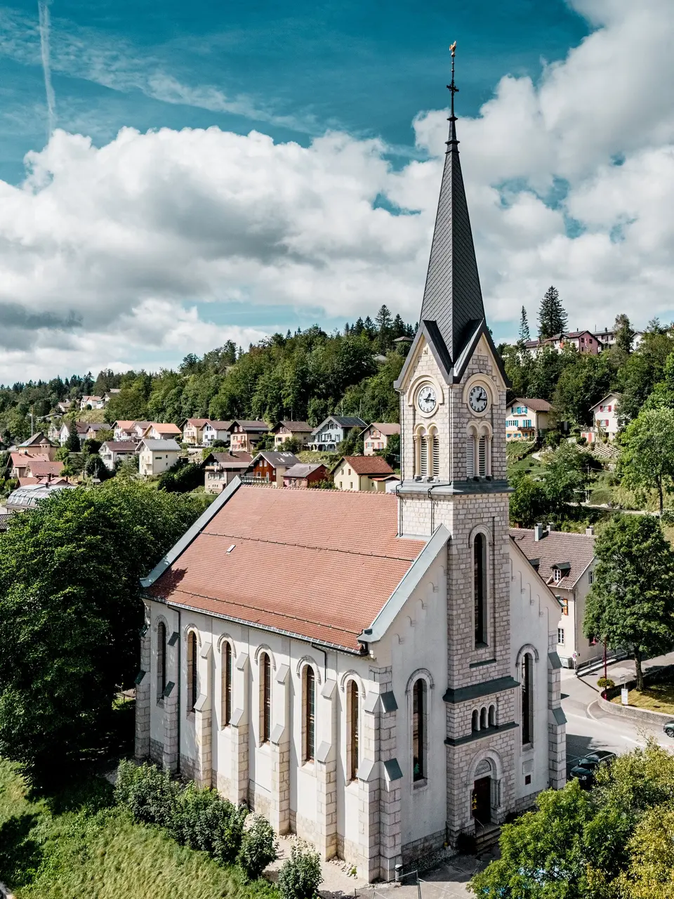 Historische Kirche in Le Sentier, Schweiz, mit markanter Turmspitze aus PREFA Dachrauten 29 × 29 in P.10 Dunkelgrau. Die robuste Aluminiumdeckung setzt einen spannenden Kontrast zum hellen Naturstein und prägt das Ortsbild eindrucksvoll. PREFA Aluminium überzeugt durch Langlebigkeit, geringes Gewicht und hohe Widerstandsfähigkeit bei anspruchsvollen Dachgeometrien.