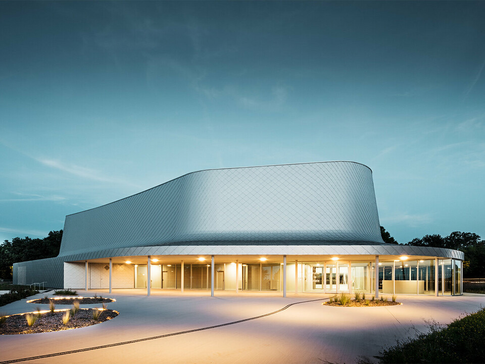 Foto di sera di un lato del palazzetto dello sport progettato dagli architetti Bohuon Bertic Architectes a Basse-Goulaine con annessa illuminazione..