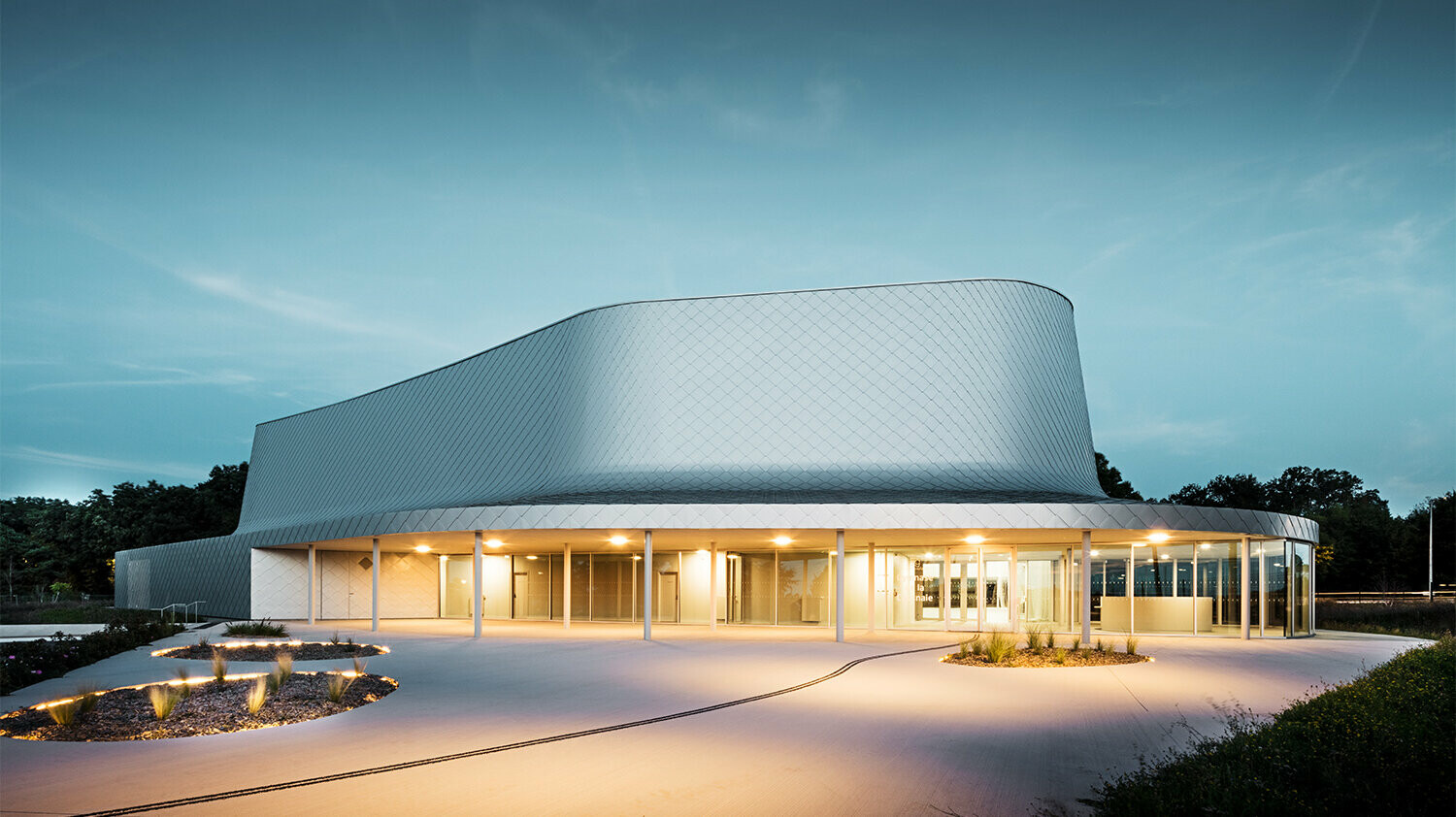 Foto di sera di un lato del palazzetto dello sport progettato dagli architetti Bohuon Bertic Architectes a Basse-Goulaine con annessa illuminazione..