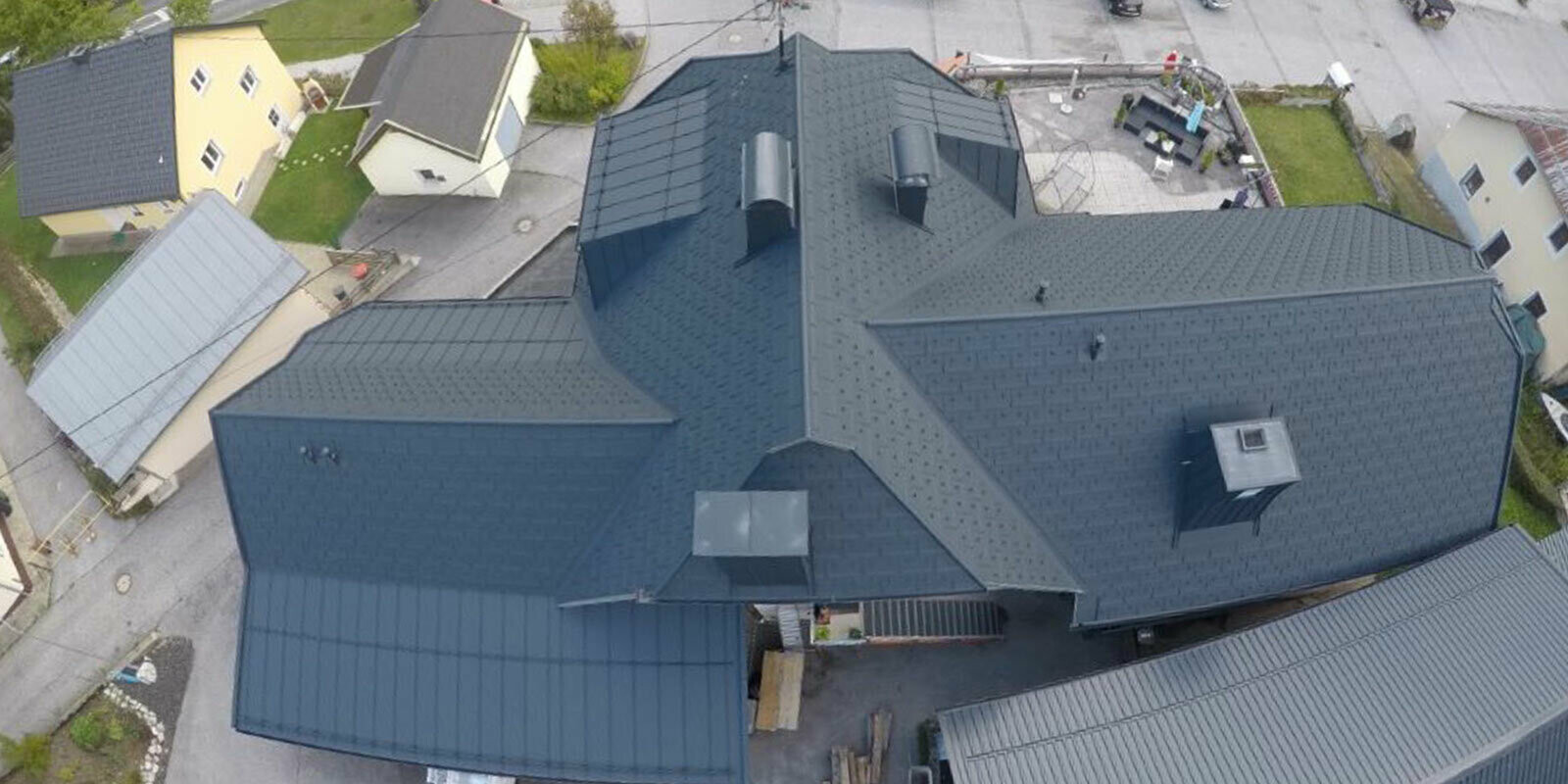 Ristrutturazione di un tetto ad ampia superficie con molti dettagli - compluvi, abbaini e camini. Il tetto è stato coperto con tegole R.16 PREFA in alluminio color antracite.