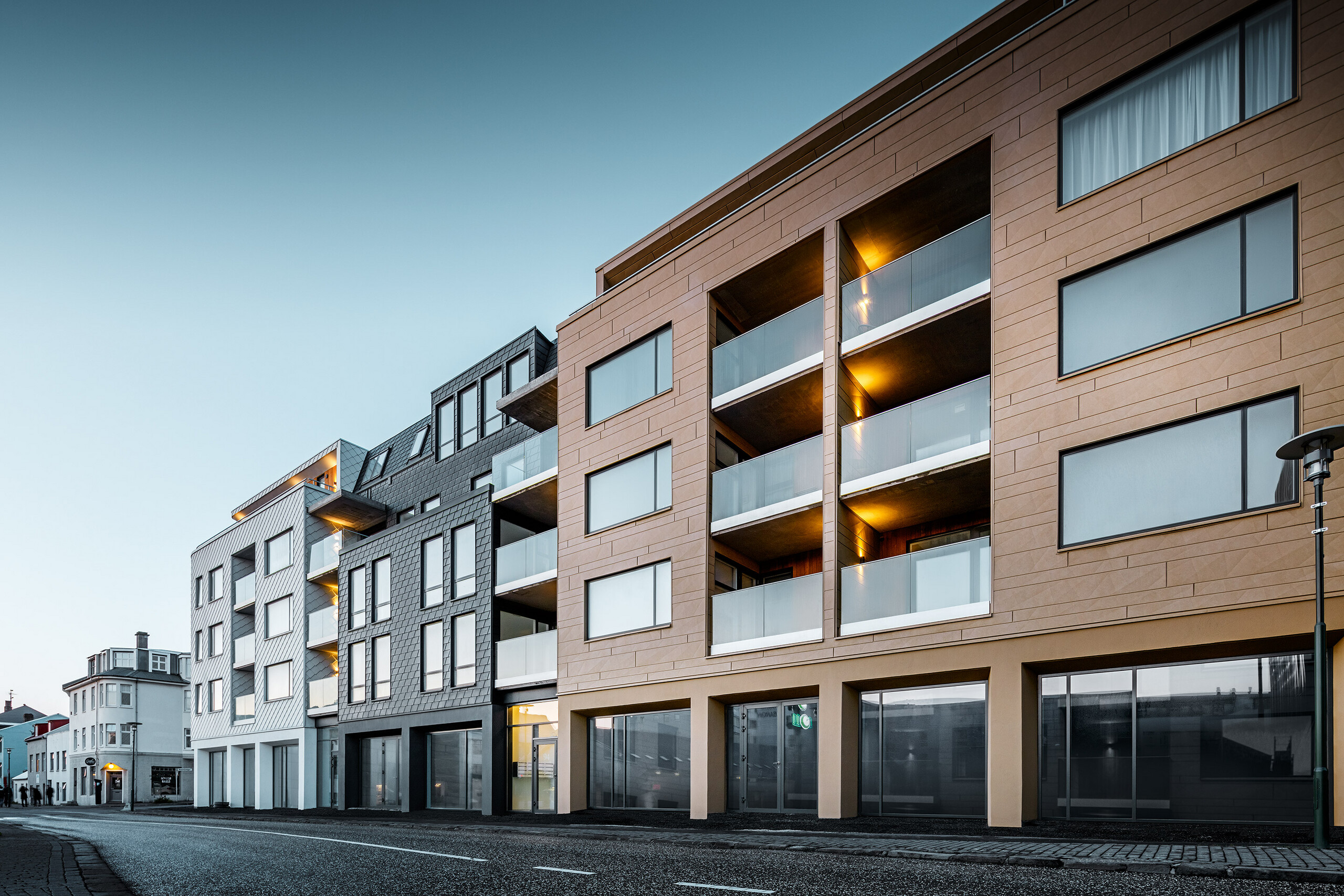 [Translate to italiano:] Seitliche Vorderansicht des Gebäudes - verkleidet mit Schindeln, Rauten und Siding.X in den Farben Weiß, Anthrazit und Sandfarben.