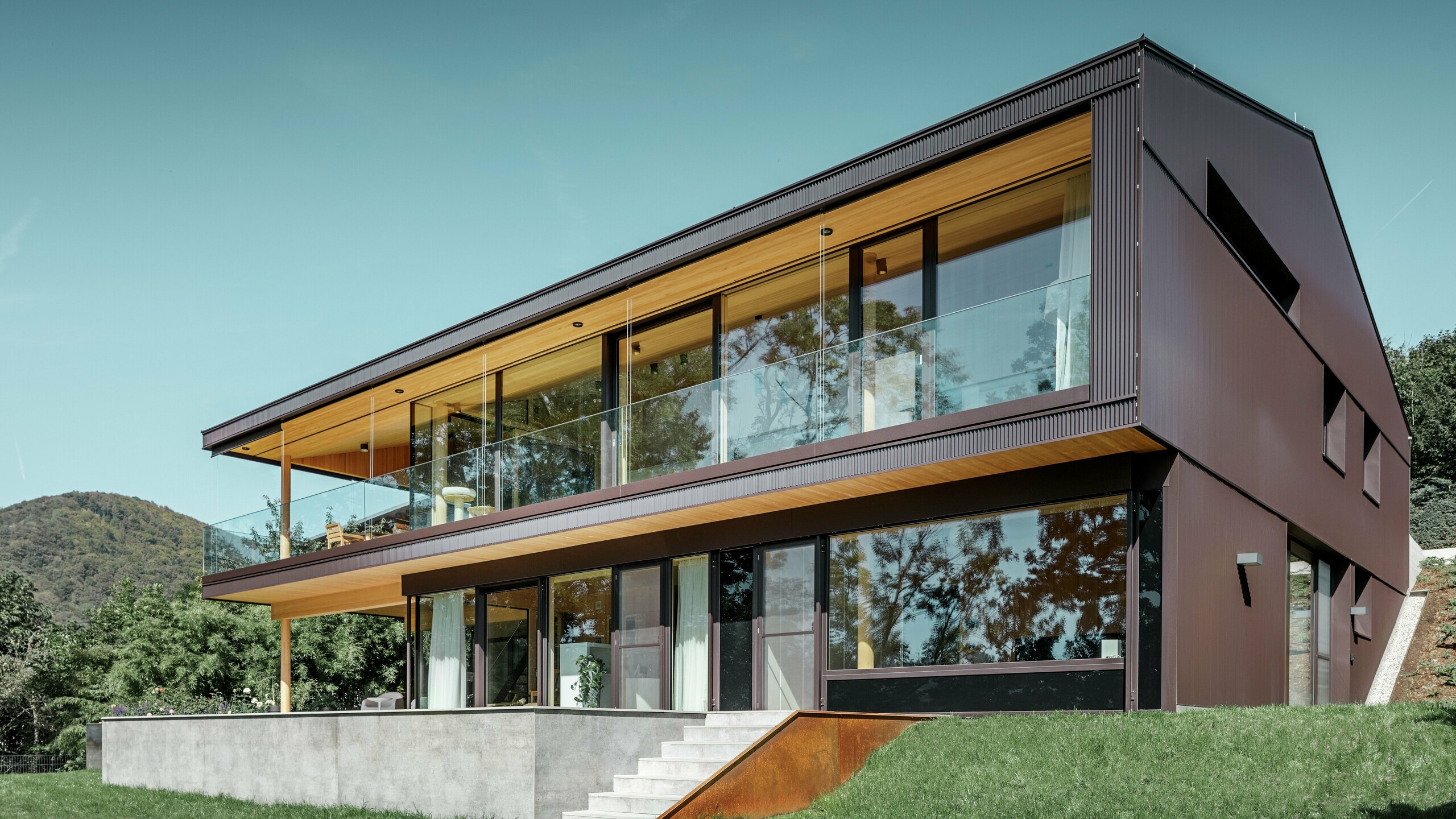 Moderna casa unifamiliare con ampie finestre lato giardino, la facciata è stata rivestita con il profilo a zeta PREFA in marrone scuro.