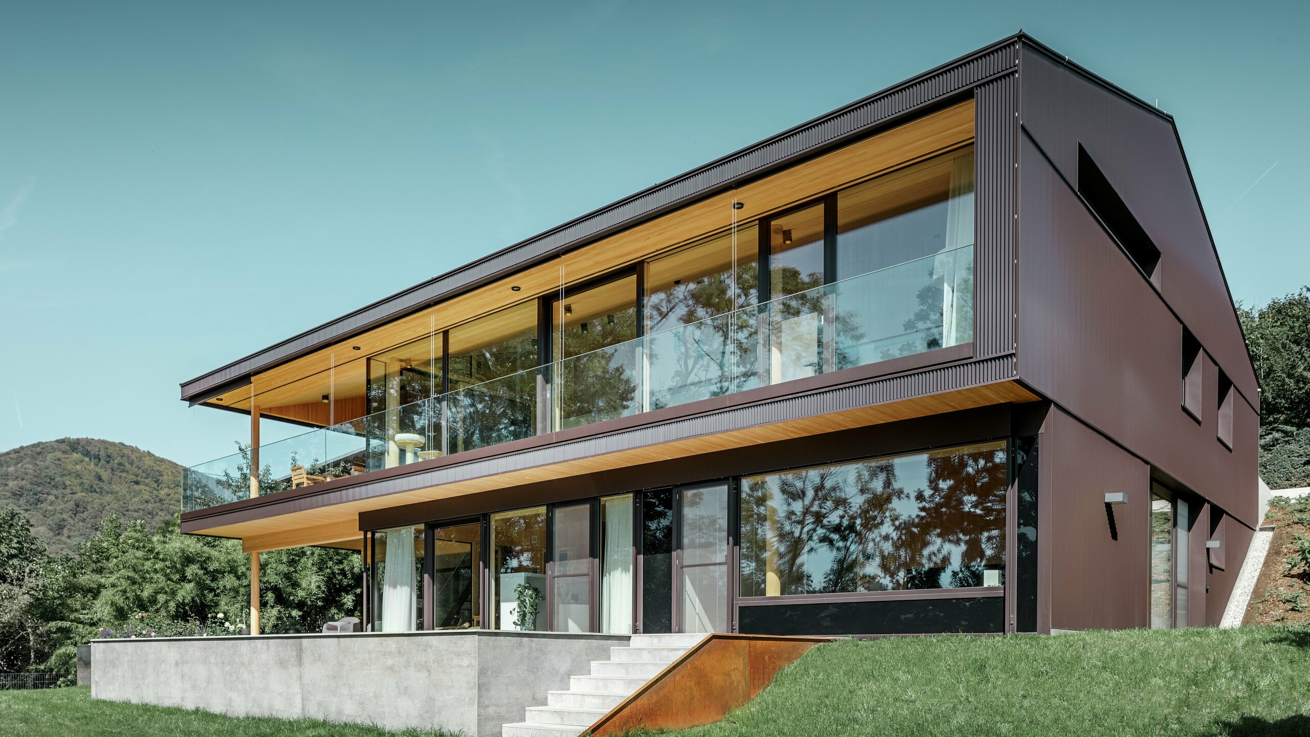 Maison individuelle moderne à grandes fenêtres côté jardin, dont la façade a été recouverte de profils triangle PREFA couleur brun foncé.