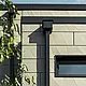Maison individuelle moderne avec toit plat et fenêtres fines. La façade est revêtue du Siding.X de façade PREFA style plissé, dans la couleur bronze. Les raccordements sont couleur anthracite. Le tuyau de descente carré PREFA et la boîte à eau assortie couleur anthracite constituent le système de gouttières.