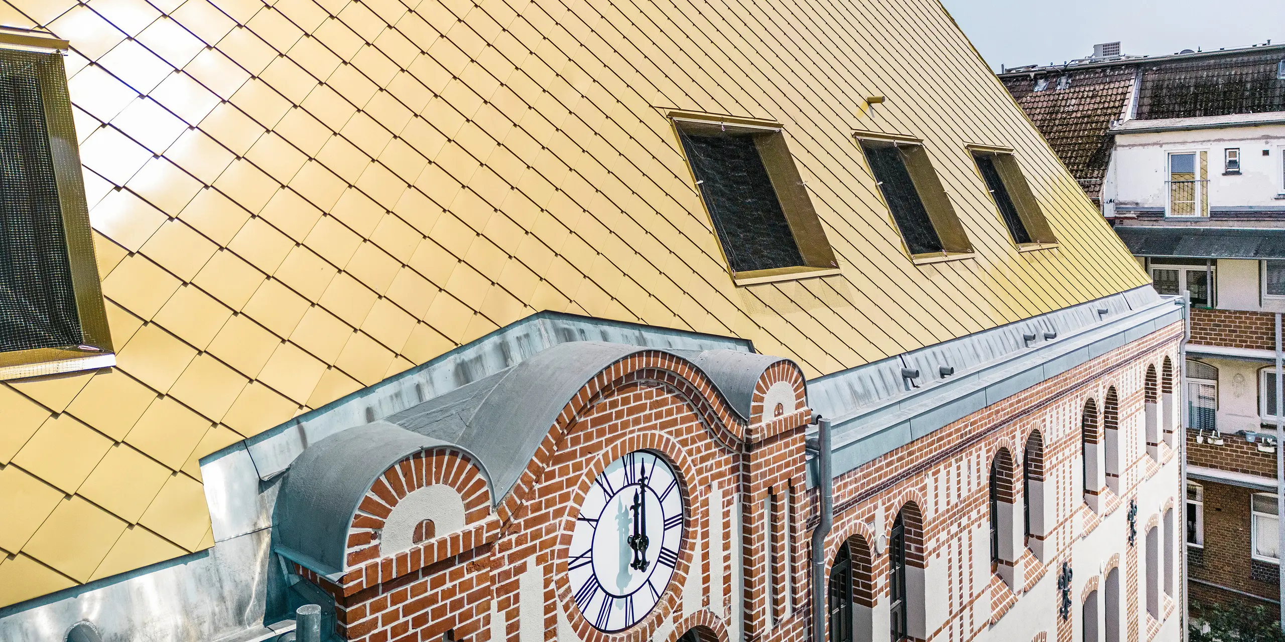 Nahaufnahme der speziellen Dachlandschaft des Studentenwohnheims "The Station" in Kiel. Das Gebäude wurde mit PREFA Dach- und Wandrauten 29 × 29 in der Farbe Mayagold verkleidet.