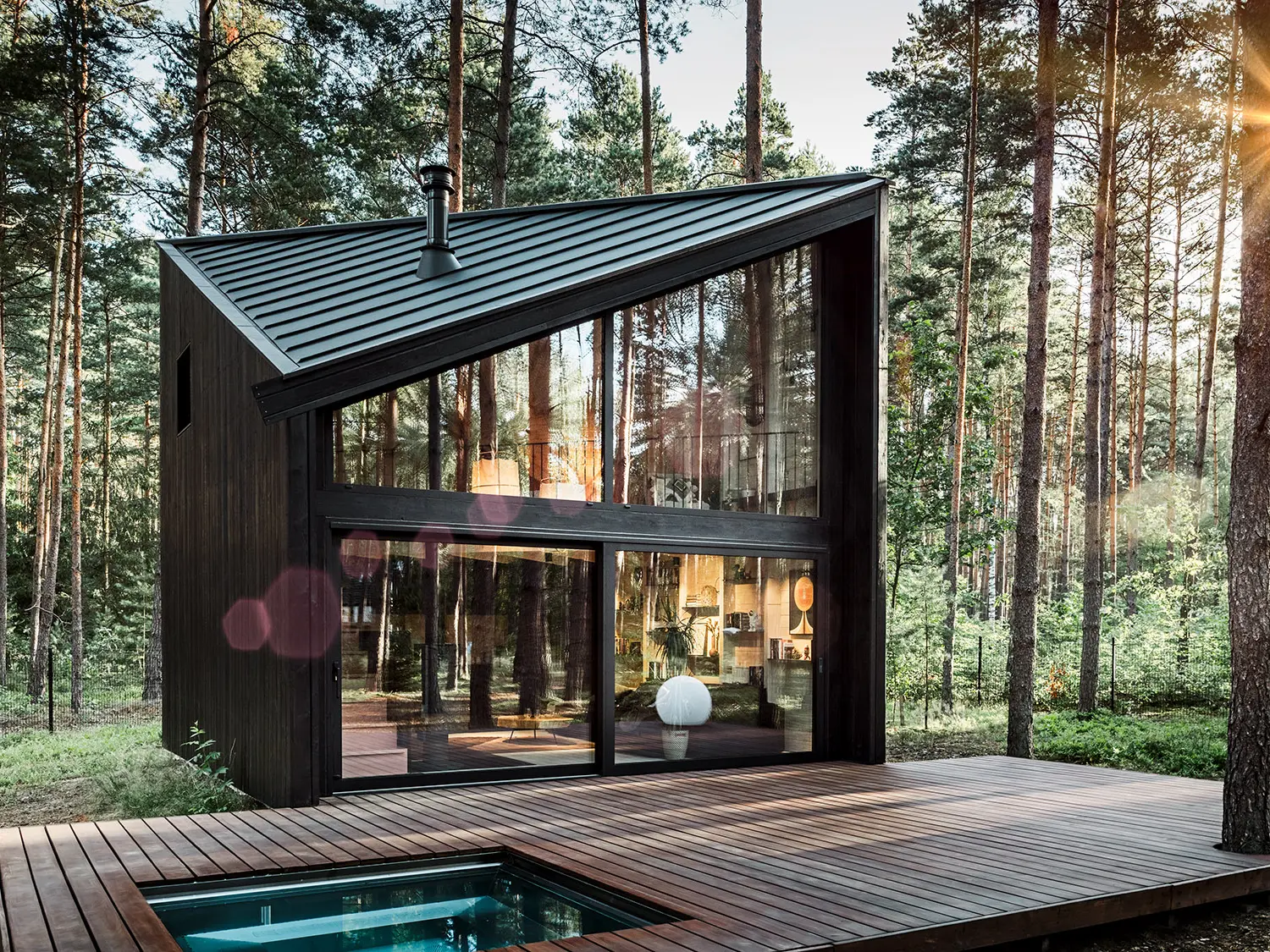 Seitenansicht eines Ferienhauses mit schrägem Prefalz-Dach. Die umgebende Natur spiegelt sich im verglasten Bereich wider.