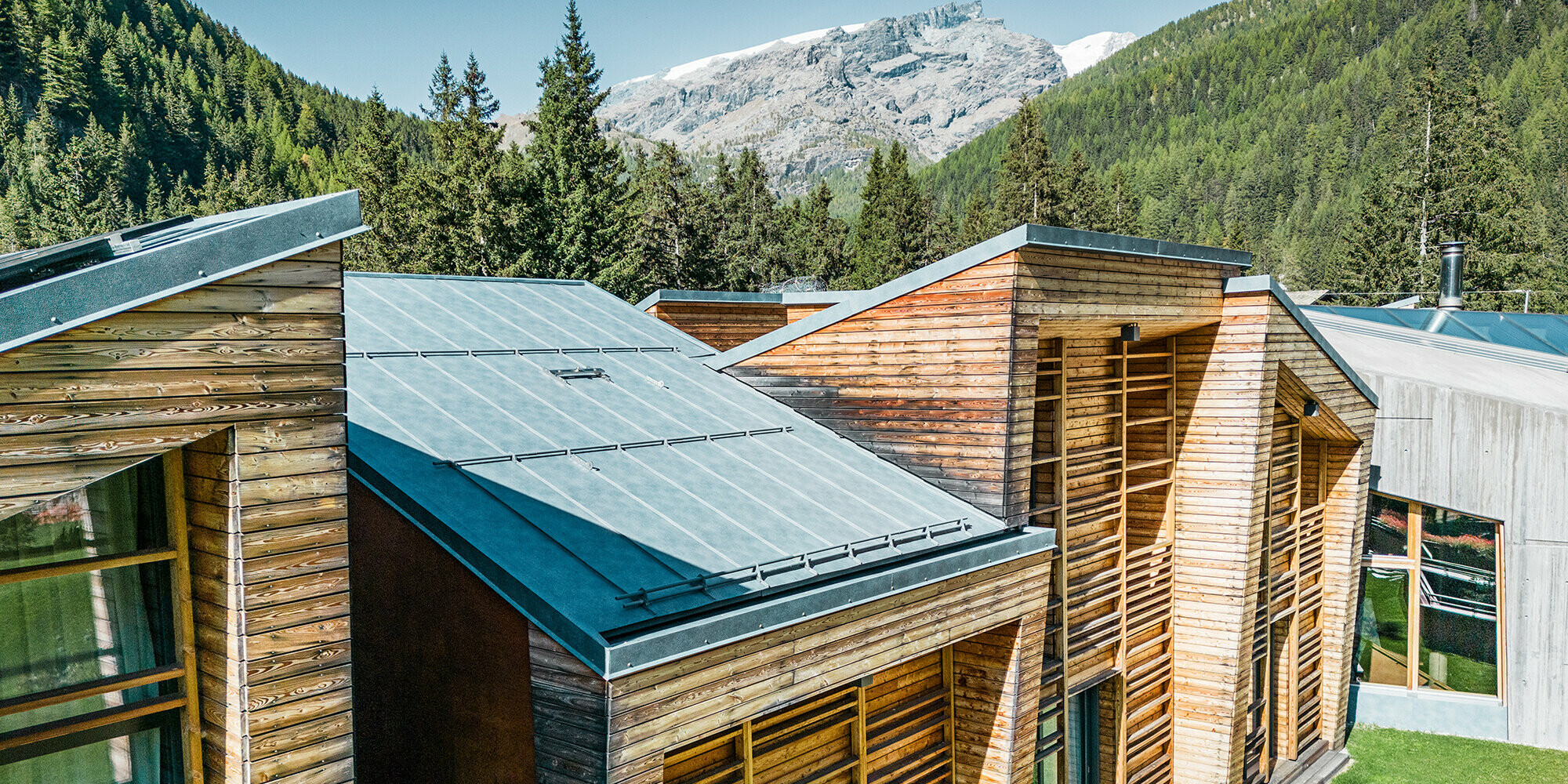 Seitliche Detailansicht der Dachlandschaft, die Holzfassade und die sorgfältig verlegten Prefalz Bahnen sind gut sichtbar.