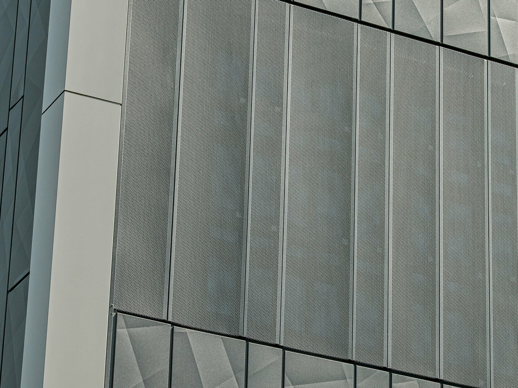 Vista della facciata di un negozio Eurospar a Rohrbach con rivestimento PREFA Siding.X e doghe perforate nel colore antracite. Gli elementi doga.X presentano un vivace disegno geometrico delle fughe, mentre le doghe perforate offrono una struttura moderna e traspirante.