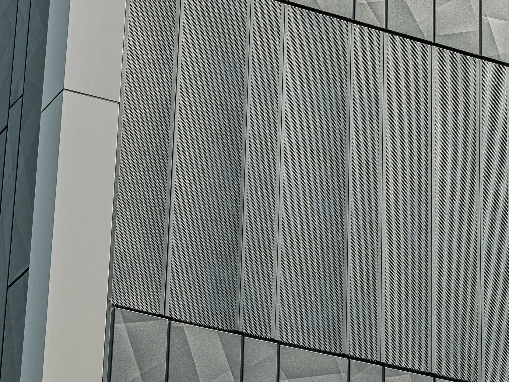 Vista della facciata di un negozio Eurospar a Rohrbach con rivestimento PREFA Siding.X e doghe perforate nel colore antracite. Gli elementi doga.X presentano un vivace disegno geometrico delle fughe, mentre le doghe perforate offrono una struttura moderna e traspirante.