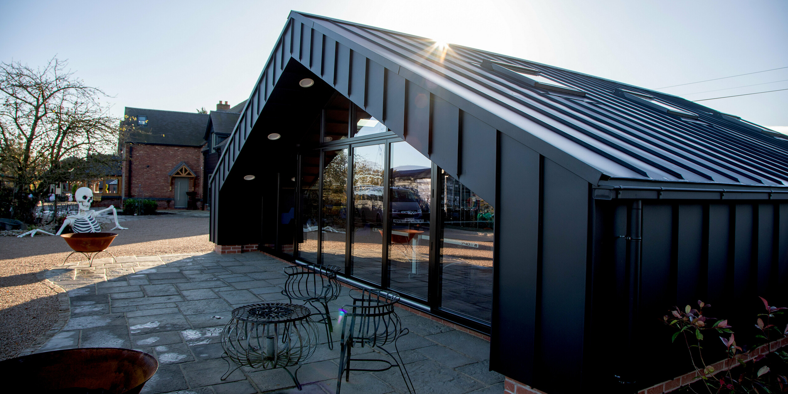 Architektonische Außenansicht des modernen Freizeitgebäudes mit vollständig mit PREFALZ in P.10 Schwarz verkleideter PREFA Aluminiumhülle. Die präzisen Stehfalzlinien, die großzügige Glasfront und die kantige Dachform erzeugen ein dynamisches, hochwertiges Erscheinungsbild. Die robuste, witterungsbeständige Aluminiumoberfläche sorgt für maximale Langlebigkeit und setzt klare architektonische Akzente im Außenbereich.