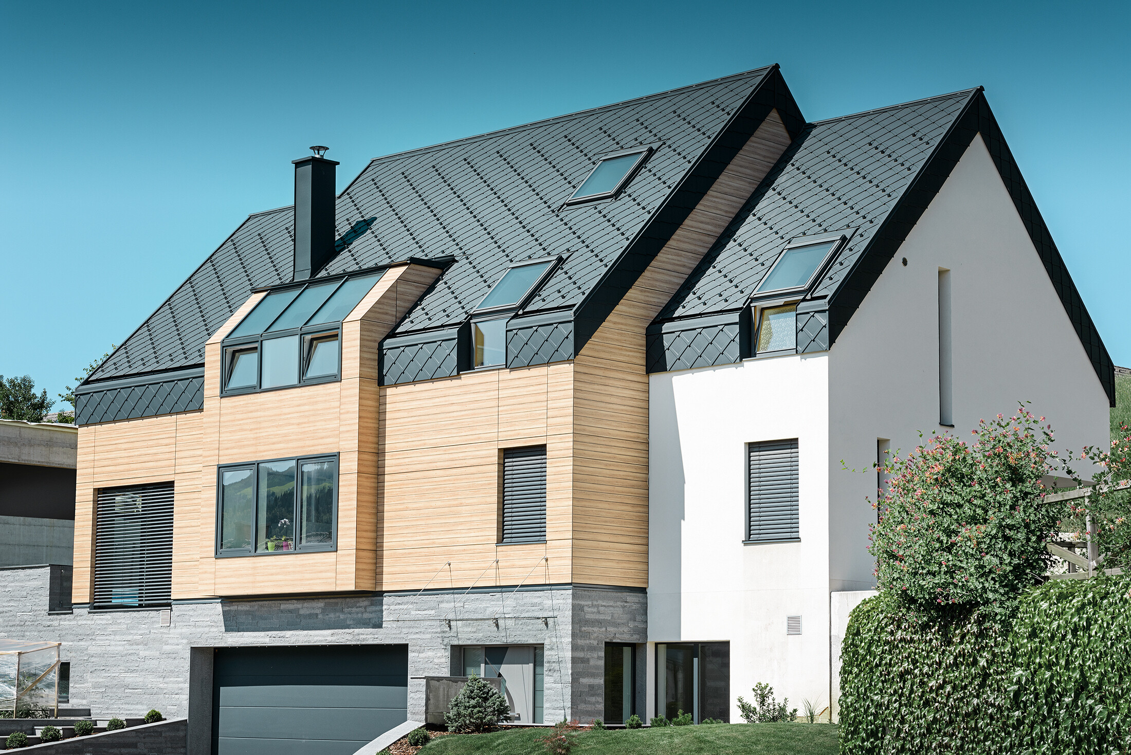 Nuova costruzione in stile contemporaneo, in cui il manto di copertura si estende oltre la parte superiore della facciata. Come copertura è stata utilizzata la scaglia in alluminio in antracite