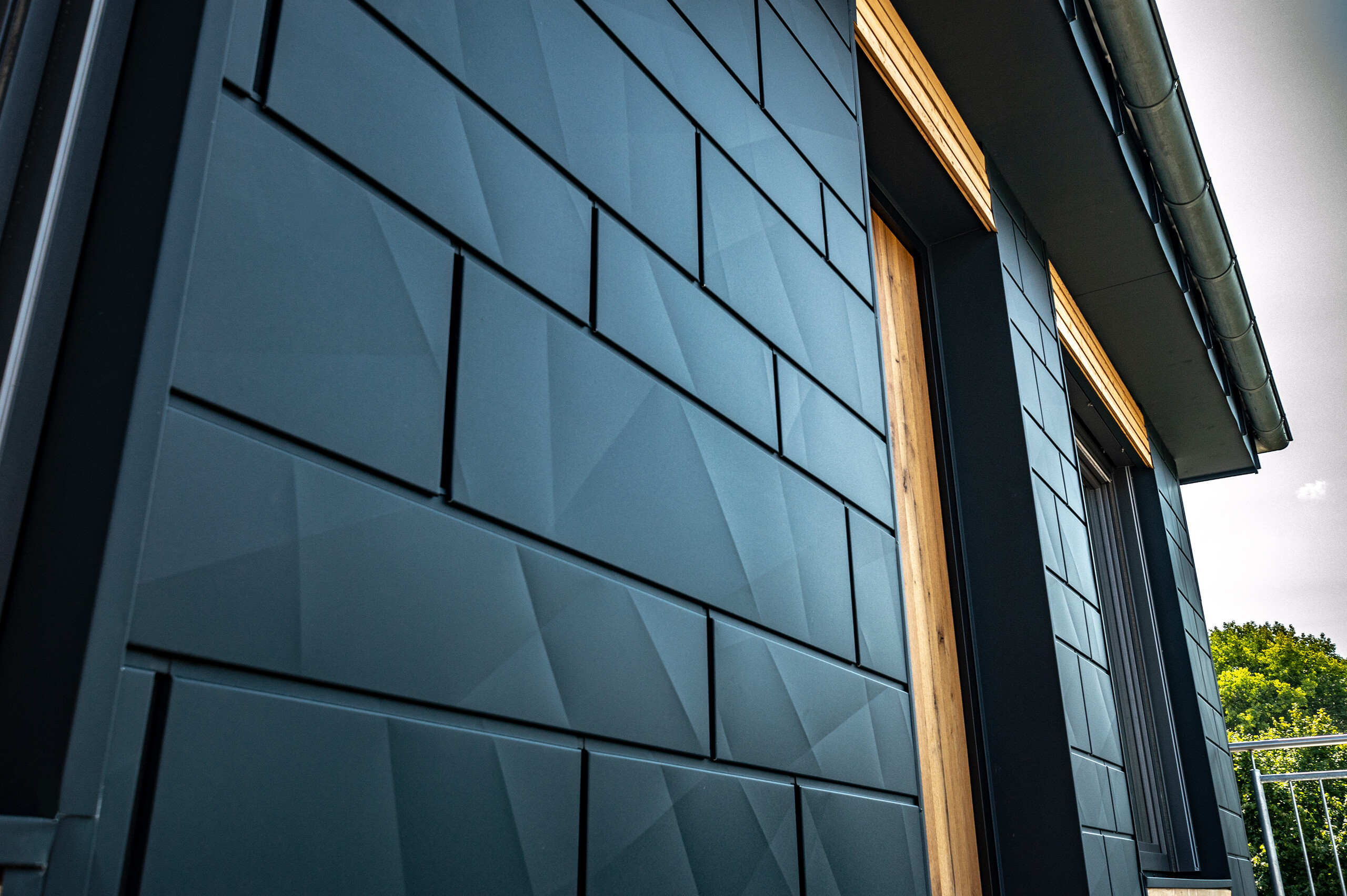 Fassade mit PREFA Siding.X in Anthrazit mit Balkontüren und großen Glasflächen gemischt mit einer Holzfassade.