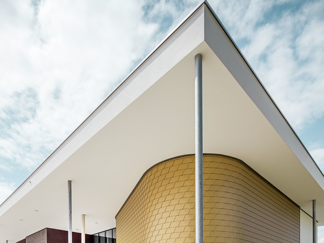 Seitliche Aufnahme der Landesmusikschule in Buchkirchen. Die Fassade wurde mit PREFA Wandschindeln in der Sonderfarbe Mayagold verkleidet.