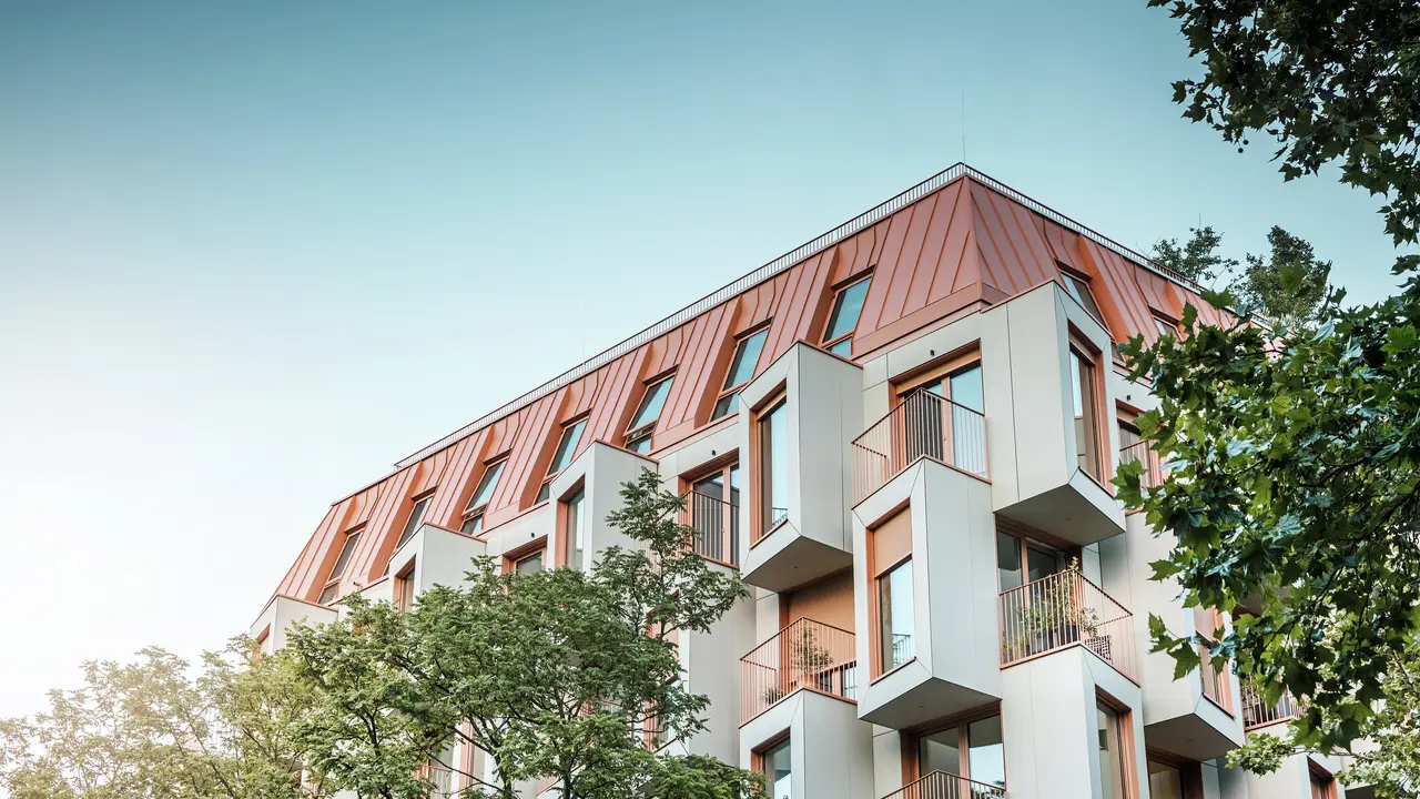 Moderna architettura residenziale nel progetto Van B a Monaco di Baviera, con un'innovativa facciata e il suggestivo tetto in alluminio PREFALZ nel colore speciale IGP Orange HDP di PREFA.  Il materiale di alta qualità del tetto convince per l'estrema durata, l'elevata resistenza e la solidità del colore. In combinazione con il design cubico della facciata e le ampie superfici vetrate, si crea un quadro d'insieme armonioso che combina funzionalità, design e sostenibilità ai massimi livelli, ideale per la vita urbana.