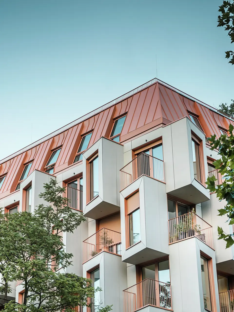 Moderna architettura residenziale nel progetto Van B a Monaco di Baviera, con un'innovativa facciata e il suggestivo tetto in alluminio PREFALZ nel colore speciale IGP Orange HDP di PREFA.  Il materiale di alta qualità del tetto convince per l'estrema durata, l'elevata resistenza e la solidità del colore. In combinazione con il design cubico della facciata e le ampie superfici vetrate, si crea un quadro d'insieme armonioso che combina funzionalità, design e sostenibilità ai massimi livelli, ideale per la vita urbana.