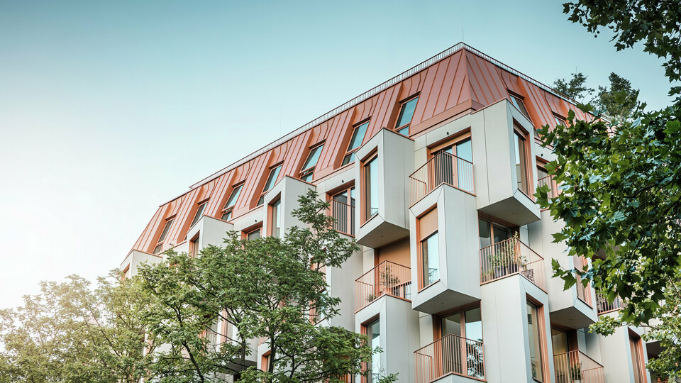 Architecture résidentielle moderne dans le projet Van B à Munich avec une façade en baie vitrée innovante et un toit en aluminium PREFALZ remarquable dans la couleur spéciale IGP Orange HDP de PREFA. Le matériau de toiture de haute qualité impressionne par son extrême durabilité, sa grande résistance et sa solidité des couleurs. En combinaison avec la conception cubique de la façade et les grandes surfaces vitrées, une image globale harmonieuse est créée qui combine fonctionnalité, design et durabilité au plus haut niveau - idéal pour la vie urbaine.