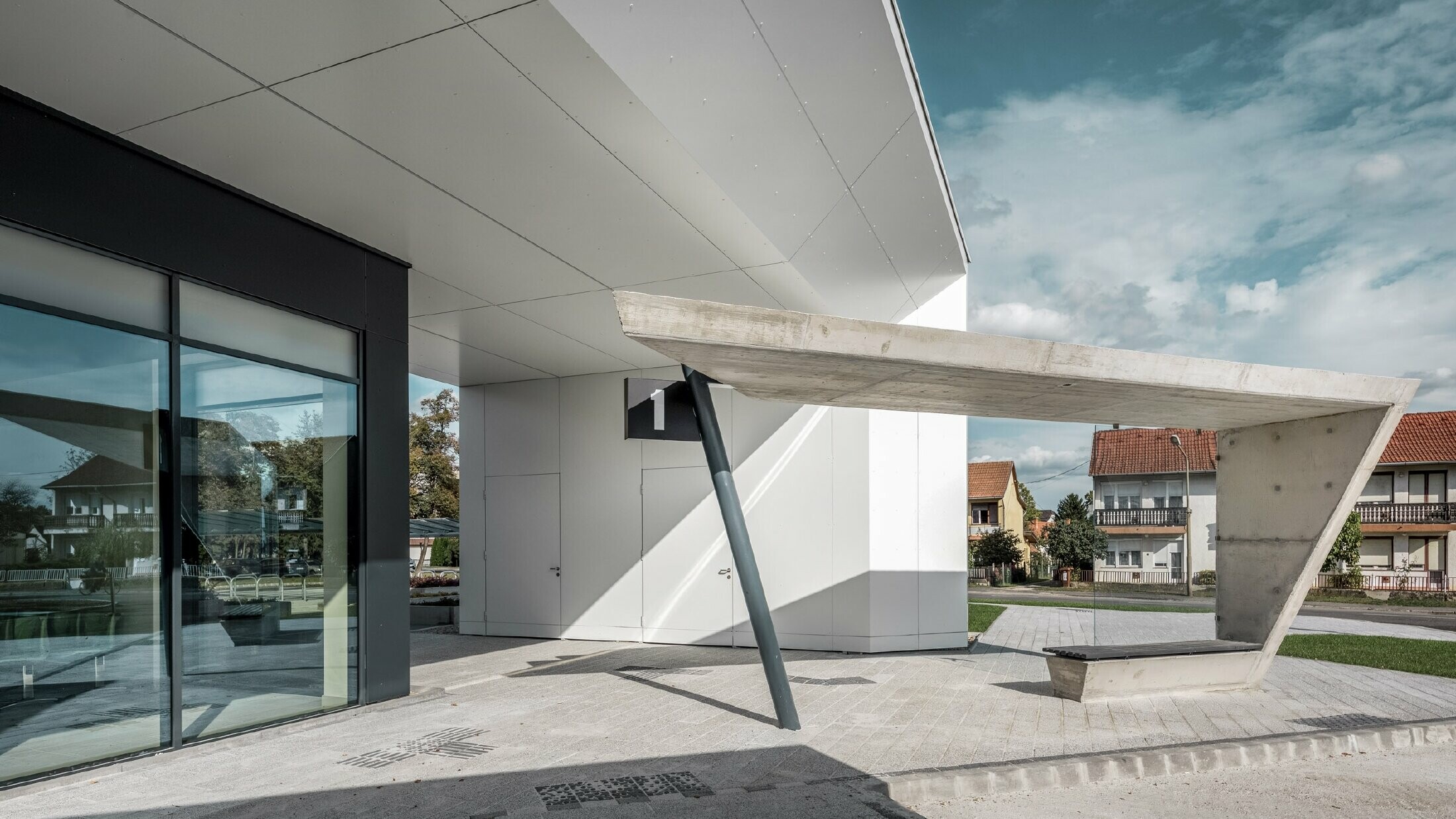 Eingangsbereich des Busbahnhofs Lenti; die Untersicht der Überdachung ist mit der PREFABOND Aluminium Verbundplatte von PREFA in Reinweiß verkleidet, die Fassadenelemente bei den Eingangstüren und Schaufenstern ist in P.10 anthrazit verkleidet.