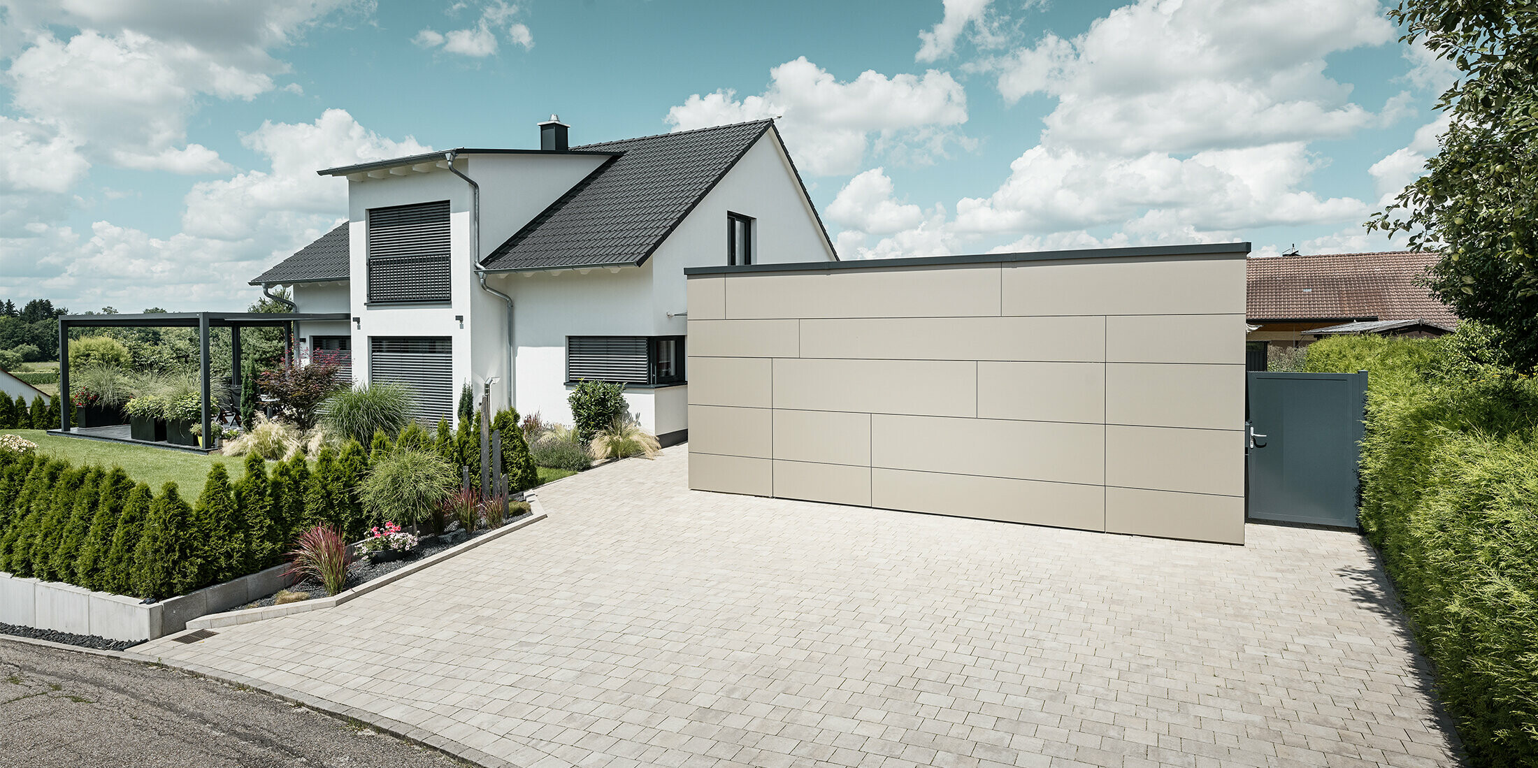 Die Garage des Einfamilienhauses ist an der Fassade komplett mit der Aluminium Verbundplatte in Bronze verkleidet. Auch das Garagentor ist mit den Fugen nicht erkennbar. Davor ist eine großzügige Einfahrt. 