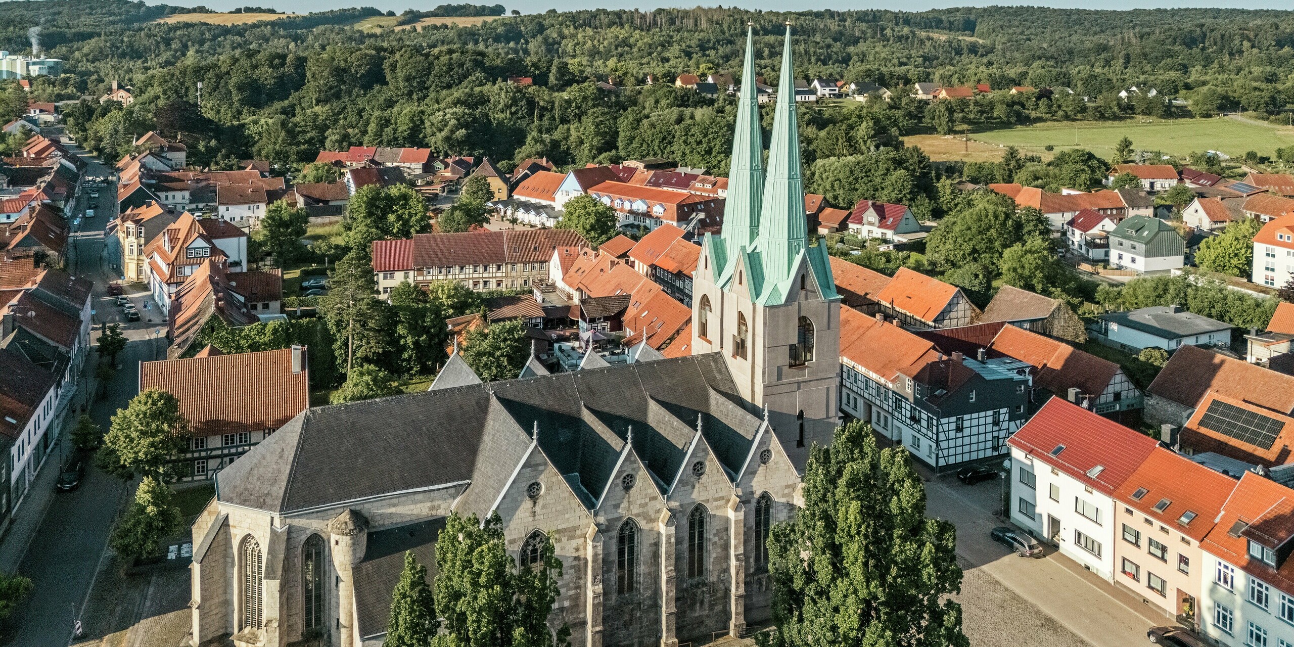 Vue aérienne grand angle de l'église Saint-Jean d'Ellrich, nichée au cœur du paysage historique de la ville. Les flèches récemment construites, revêtues de PREFALZ vert de gris P.10, sont particulièrement remarquables et contrastent élégamment avec l'environnement traditionnel. La toiture en aluminium résistant aux intempéries allie technologie moderne et design respectueux du patrimoine – un véritable atout pour le centre-ville.