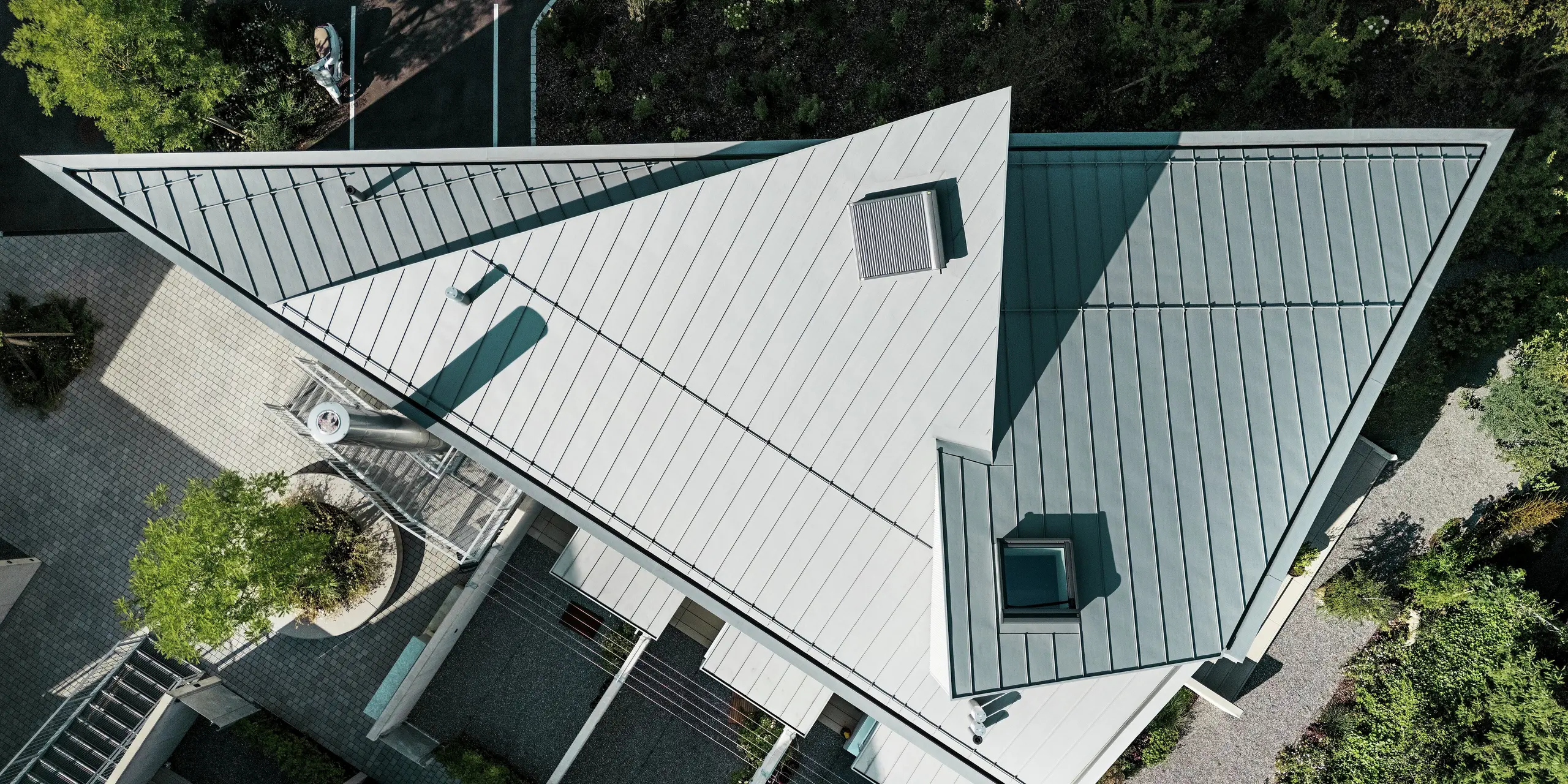 Draufsicht auf das markant gefaltete PREFALZ Dach in Patinagrau eines Tiny Homes in der Schweiz. Die präzise Ausführung in Stehfalztechnik unterstreicht die außergewöhnliche Geometrie des Baukörpers. PREFALZ überzeugt durch Flexibilität in der Gestaltung, extreme Wetterbeständigkeit und eine hochwertige Aluminium-Oberfläche für langlebige Dachlösungen.