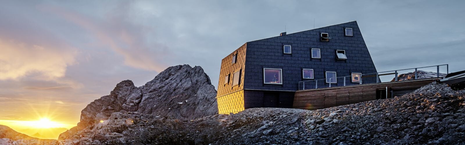 Vorderansicht der Schutzhütte am Dachstein vor einem atemberaubenden Sonnenuntergang, verkleidet mit PREFA Dach- und Fassadenpaneelen FX.12 in P10 Steingrau