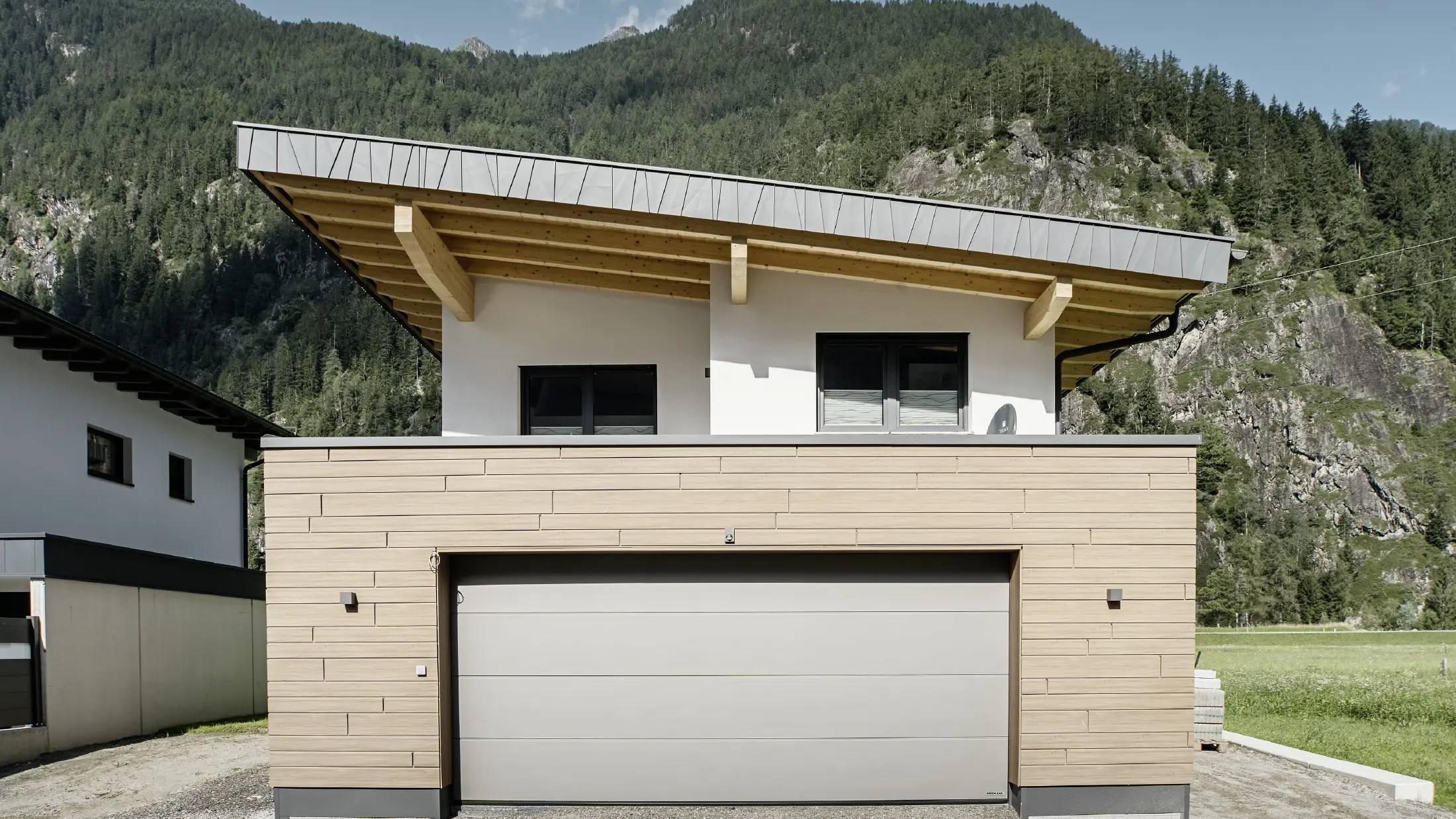 Moderna costruzione nuova con tetto a una falda e rivestimento personalizzato dei bordi del tetto, garage con tetto piano e facciata in alluminio color noce scuro di PREFA. Le doghe sono state posate in modo orizzontale con diverse larghezze utili.