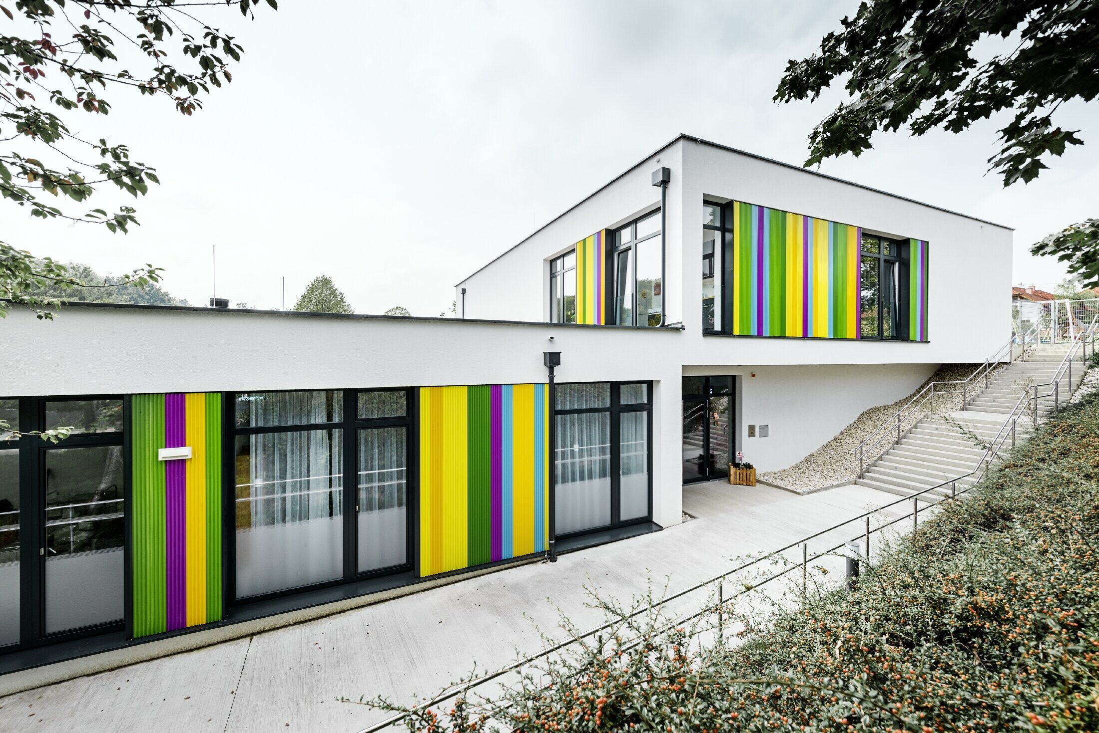 Elemento della facciata colorato di PREFA per la scuola materna ad Hargelsberg. L'edificio ha una copertura piatta e ampie finestre a tutta parete.