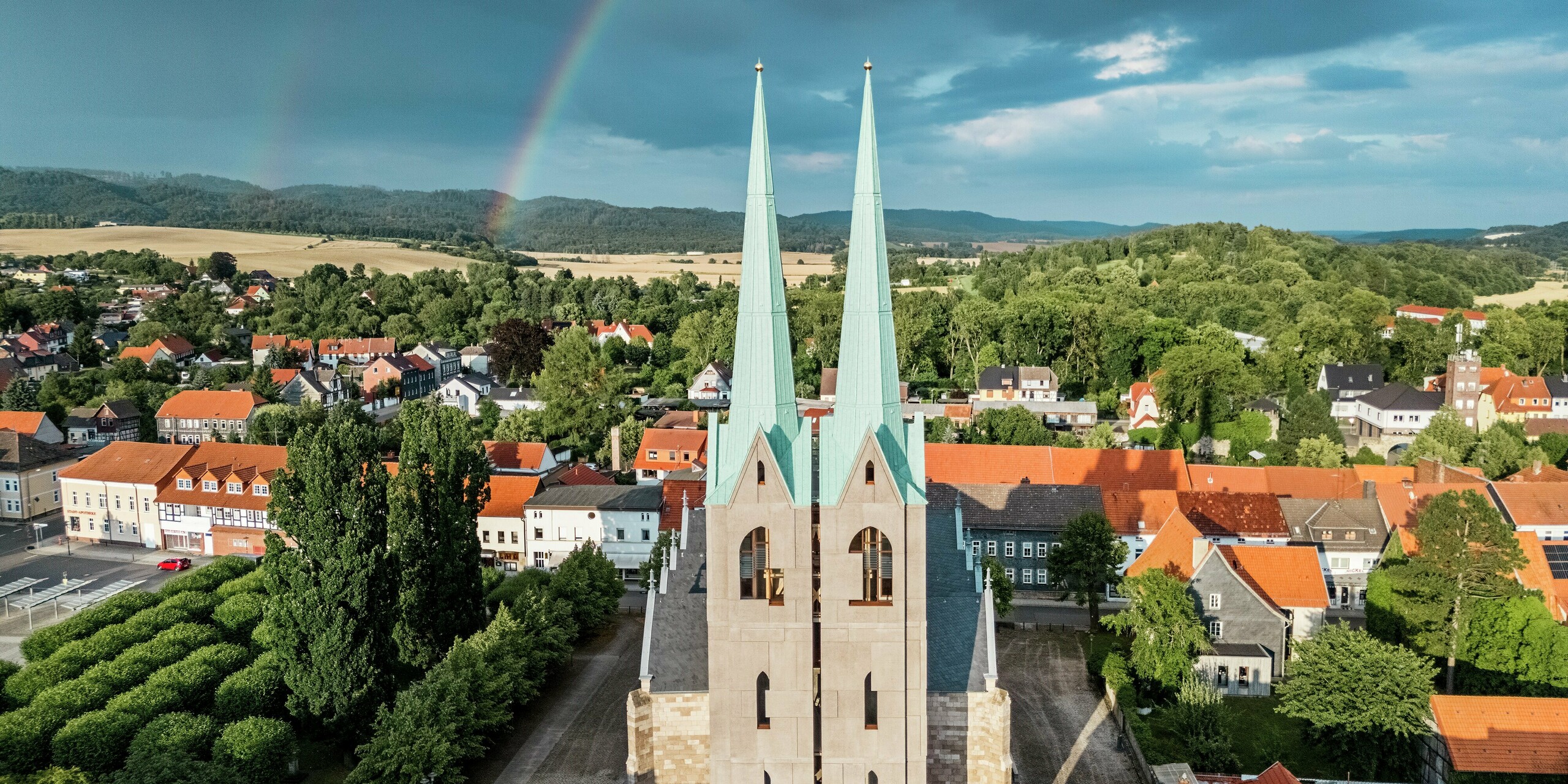 Impressionnante façade du centre touristique Ellrich, avec ses flèches remarquables en PREFALZ vert de gris P.10, se détachant sur un ciel spectaculaire et un arc-en-ciel éclatant. Malgré les nuages ​​sombres, les toitures en aluminium brillent, témoignant de la durabilité et de l'esthétique du PREFALZ, même par temps changeant. Un exemple remarquable de rénovation moderne.