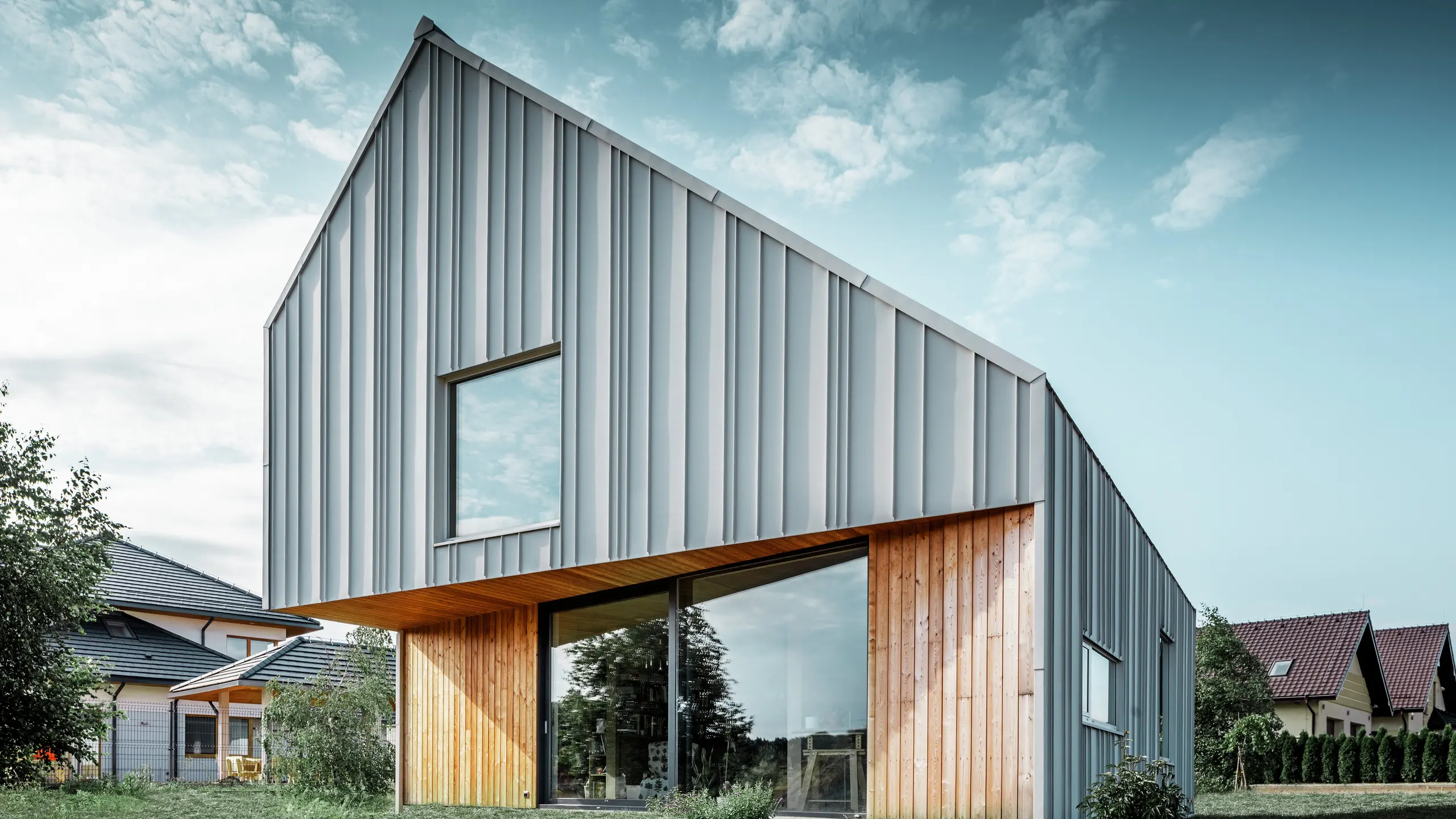 Casa unifamiliare moderna con tetto a due falde senza sporgenza e facciata in alluminio PREFA bianco. Al piano terra è stata abbinata una facciata in legno con pannelli verticali. 
