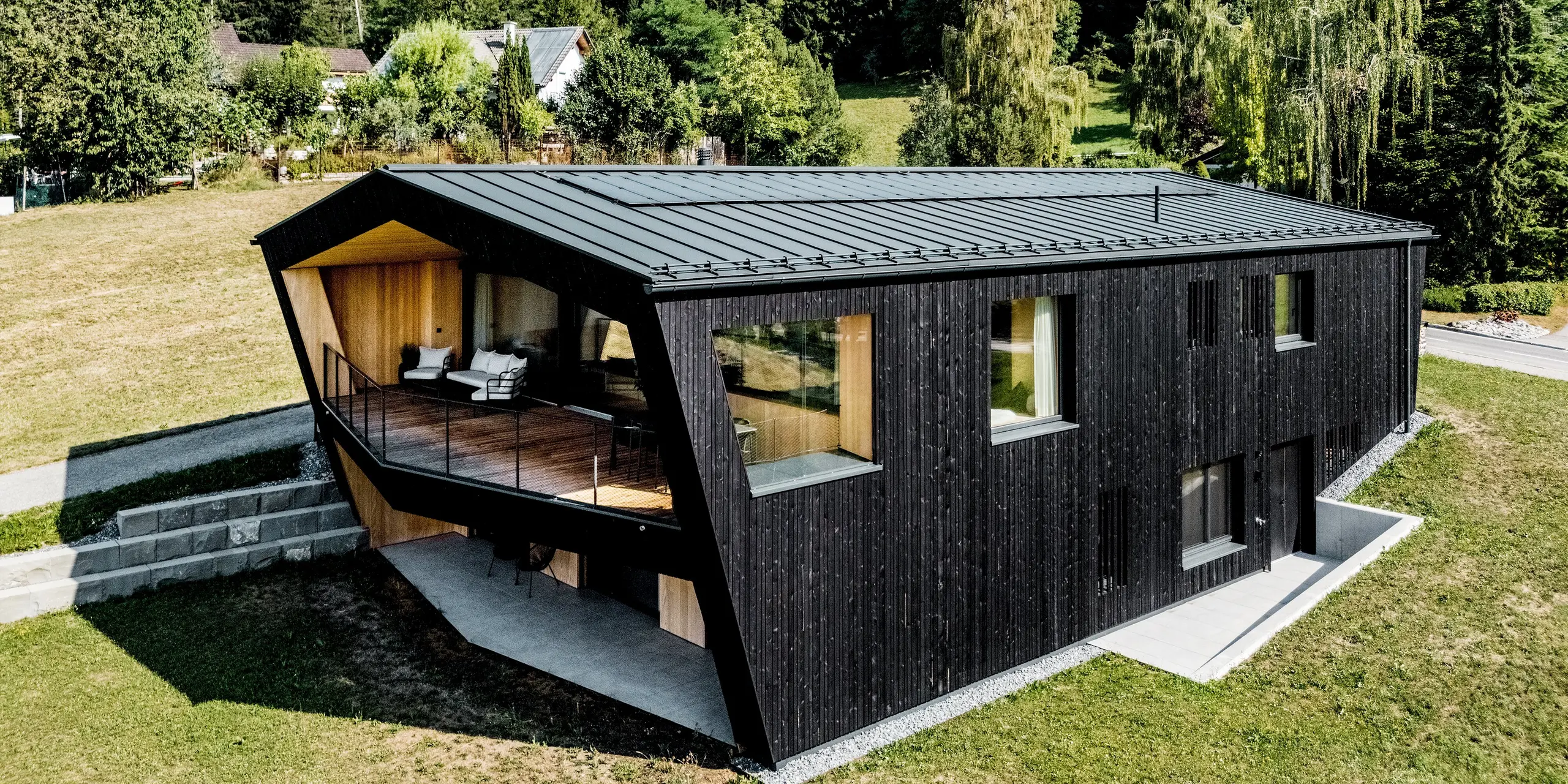 Dieses moderne Einfamilienhaus in Röthis besticht durch sein markantes Satteldach aus PREFALZ in der Farbe P.10 Anthrazit. Auf dem Dach thront zusätzlich das Solarmodul PREFALZ für nachhaltige Energiegewinnung. Die dunkle Holzfassade, die großzügigen Fenster und der außergewöhnliche Balkon mit warmer Holzverkleidung schaffen spannende Kontraste. Die langlebige, leichte und witterungsbeständige PREFA Aluminiumdeckung sowie die farblich abgestimmte Dachentwässerung vereinen moderne Architektur mit zuverlässiger Funktionalität.