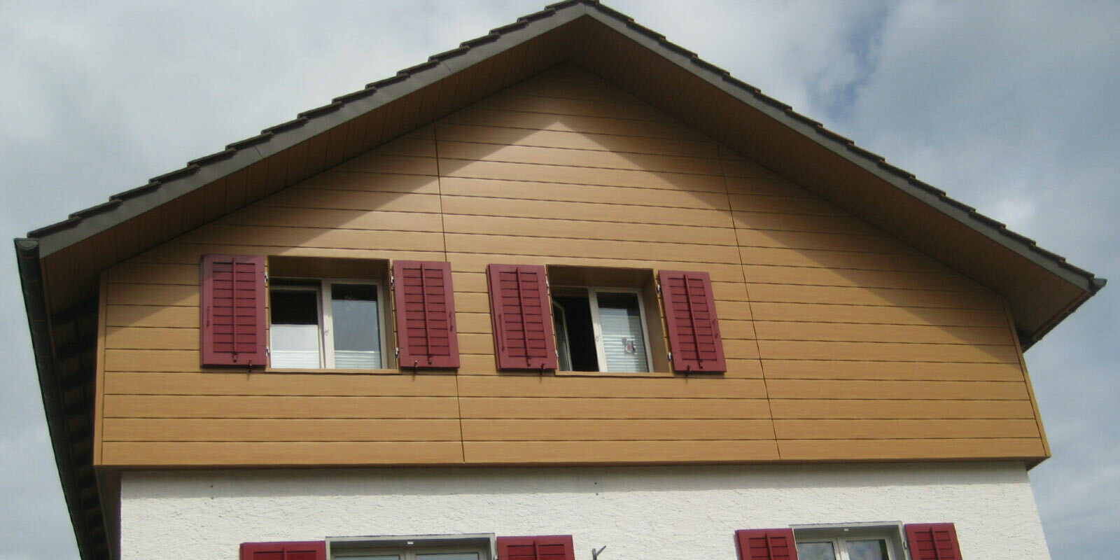 Facciata con effetto legno con doghe di rivestimento PREFA in posa orizzontale, finestre con persiane rosse