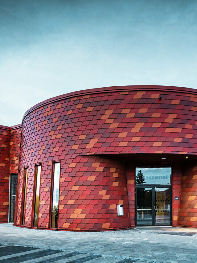 Vue de face de cette patinoire suédoise. Les bardeaux rouge oxyde s'adaptent parfaitement aux courbes du bâtiment.