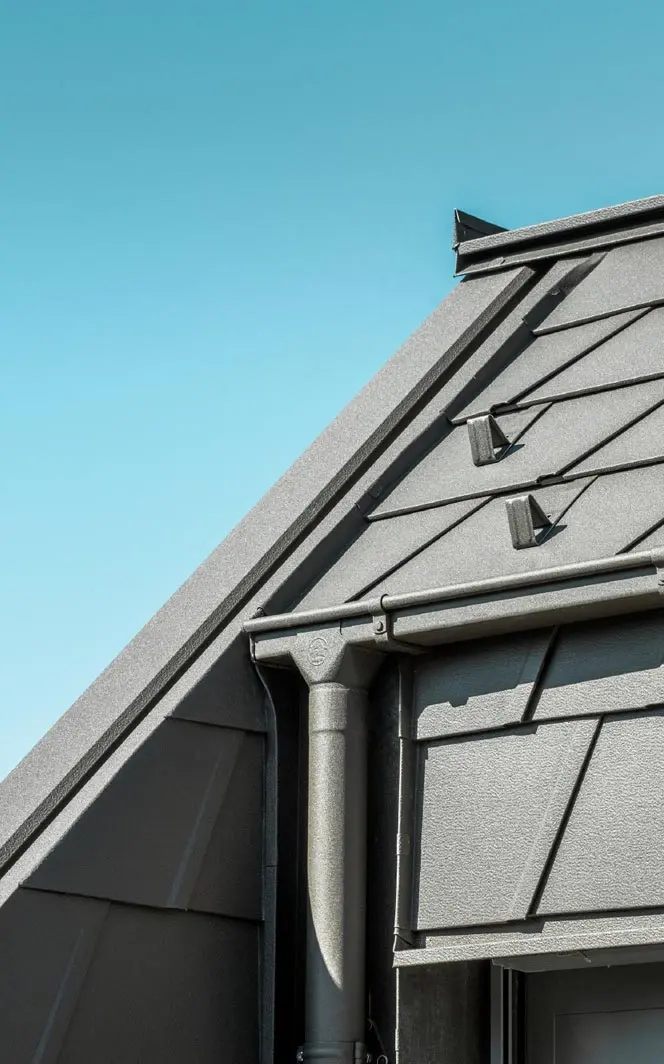 Dach mit PREFA Aluminiumdachplatten und modernen Regenrinnen, die eine hohe Langlebigkeit und ästhetische Funktionalität bieten, vor einem klaren blauen Himmel.