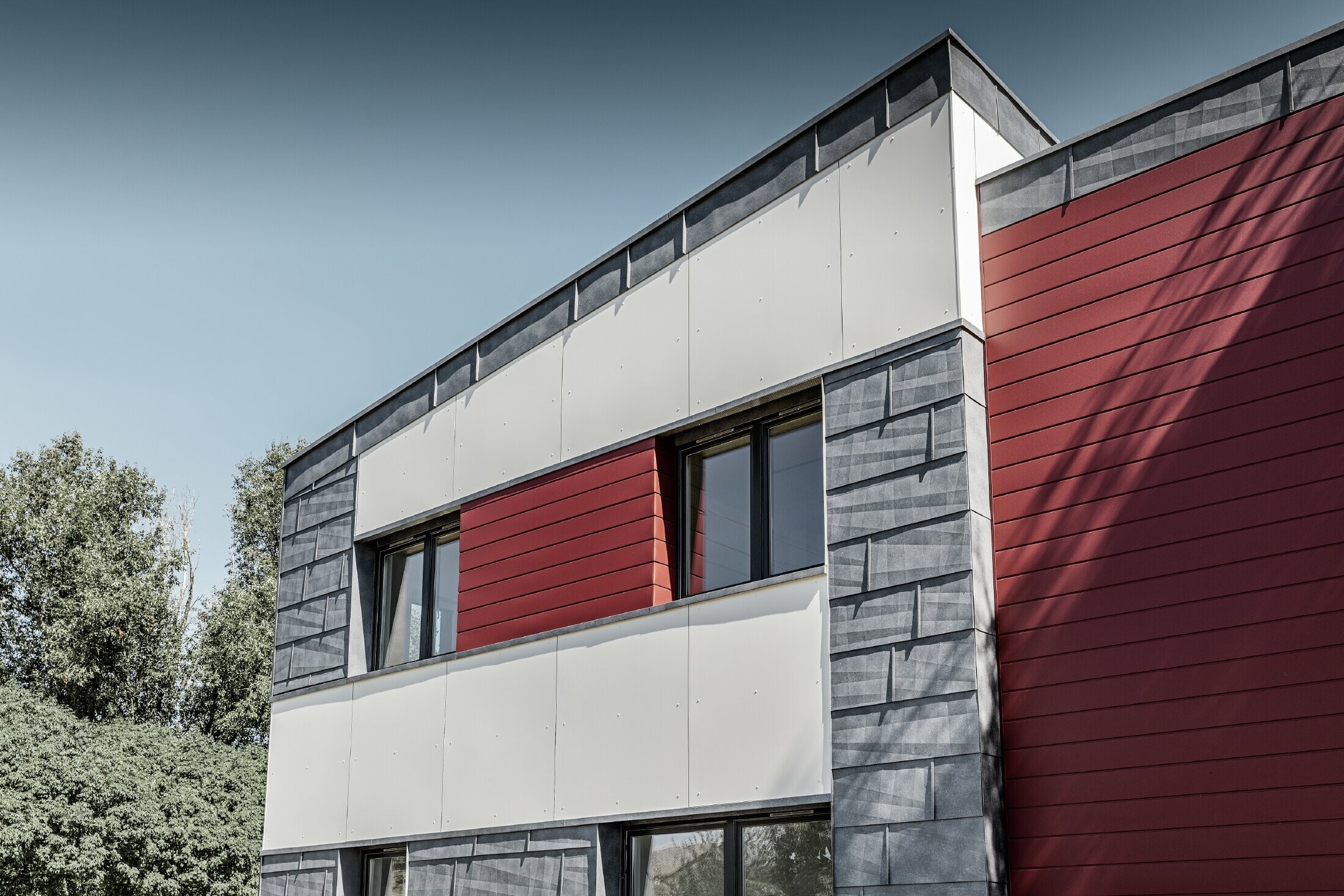 Complexe de bureaux moderne — Façade tricolore (blanc, rouge et gris pierre) réalisée à partir de produits en aluminium PREFA (sidings, panneaux de façade FX.12 et panneaux composites en aluminium)