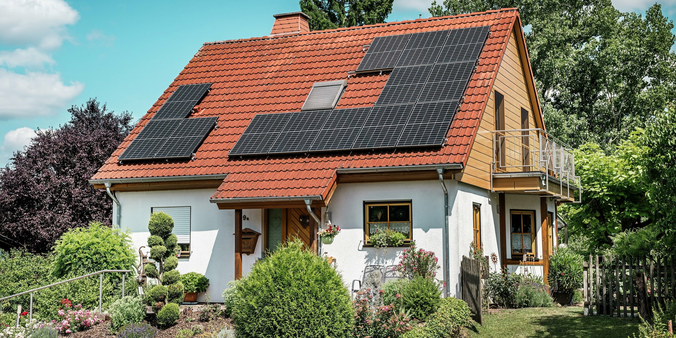 L'image présente une charmante maison individuelle à Blieskastel, dont le pignon récemment rénové, revêtu de Siding PREFA en chêne naturel, attire immédiatement le regard. L'aspect chaleureux du bois de l'aluminium s'harmonise parfaitement avec la toiture en tuiles rouges et les panneaux photovoltaïques grand format. Entourée d'un jardin soigneusement entretenu, la maison offre une impression d'ensemble lumineuse et ensoleillée. Résistant aux intempéries et inaltérable, le bardage PREFA offre l'esthétique naturelle du bois, sans aucun entretien et avec une stabilité dimensionnelle permanente. Idéal pour des rénovations de façade durables.