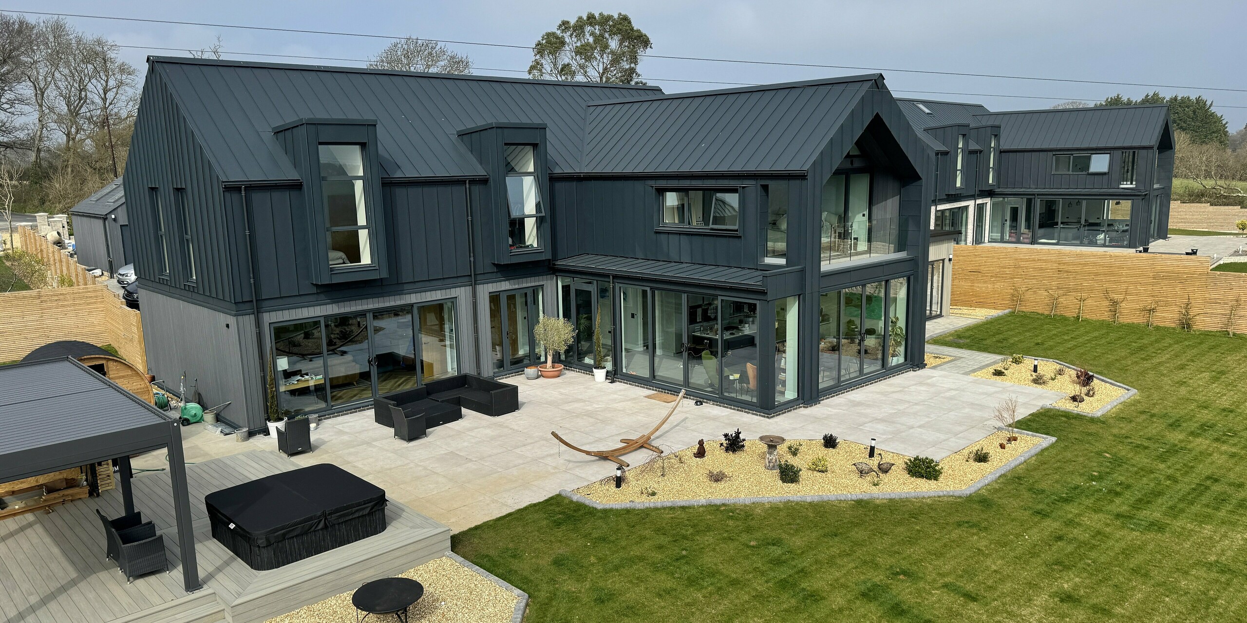 Deux maisons individuelles modernes sur l'île de Wight arborent un remarquable revêtement de toiture et de façade PREFALZ, couleur P.10 gris sombre. Leurs lignes épurées et leurs vastes façades vitrées baignent les pièces de lumière. Résistantes à la corrosion, durables et faciles d'entretien, les surfaces en aluminium sont idéales pour un environnement côtier. Au rez-de-chaussée, différents matériaux apportent des touches subtiles et confèrent à l'ensemble une personnalité unique. L'alliance d'une architecture contemporaine et des produits PREFA haut de gamme fait de ce projet un véritable chef-d'œuvre.
