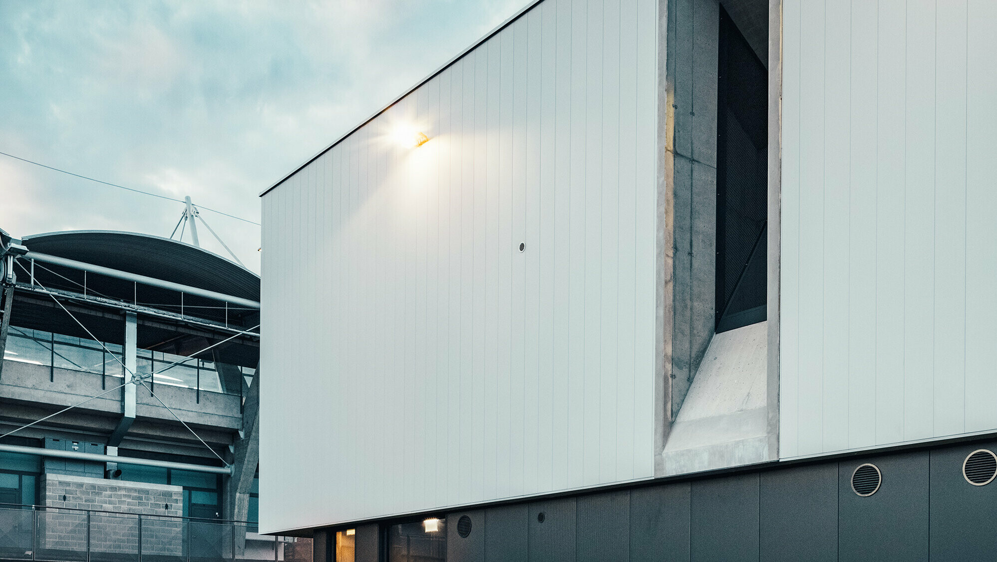 Gros plan du mur latéral avec la façade ventilée. À l’arrière-plan : le stade de football.