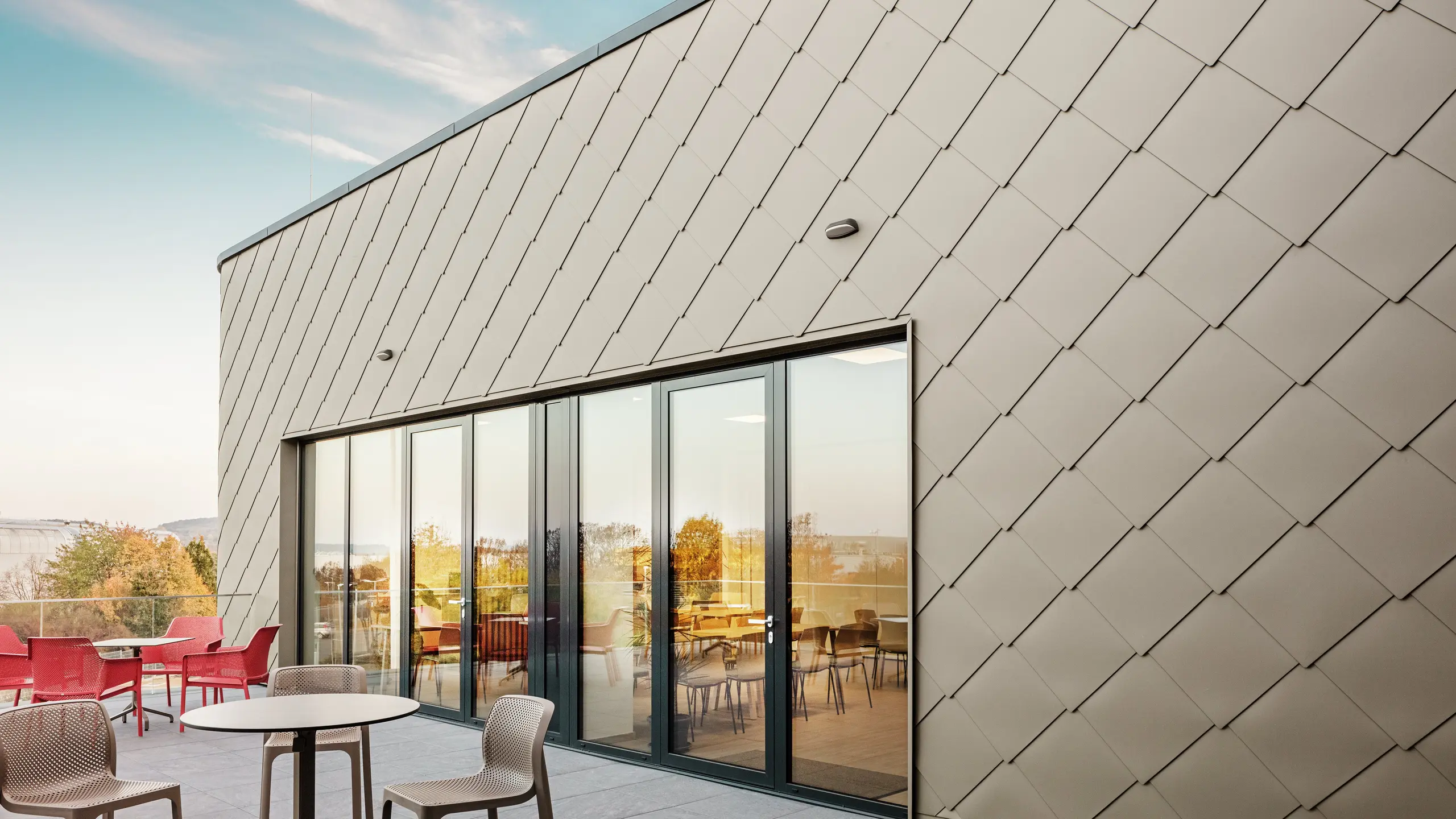 Die Fassade des neuen PREFA Standortes in Törökbálint besticht durch die eleganten PREFA Wandrauten 44 × 44 in P.10 Prefabronze. Die präzise verlegte Aluminiumfassade sorgt für ein modernes, dynamisches Erscheinungsbild und bietet gleichzeitig maximalen Schutz vor Witterungseinflüssen. Die großzügige Glasfront verbindet Innen- und Außenbereich und schafft auf der großzügigen Terrasse eine helle und einladende Atmosphäre.